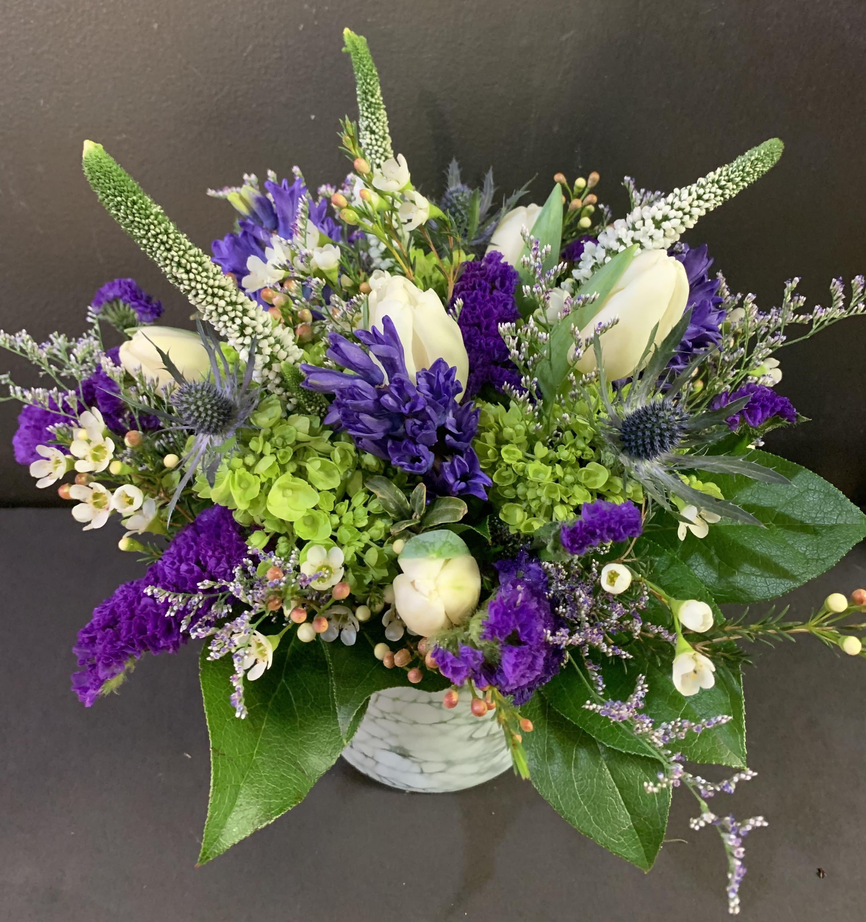 Purple Rain - Early signs of spring pop out of this beautiful seasonal purple vase. Exact flowers included may be substituted due to market availability but color and feel will stay the same.