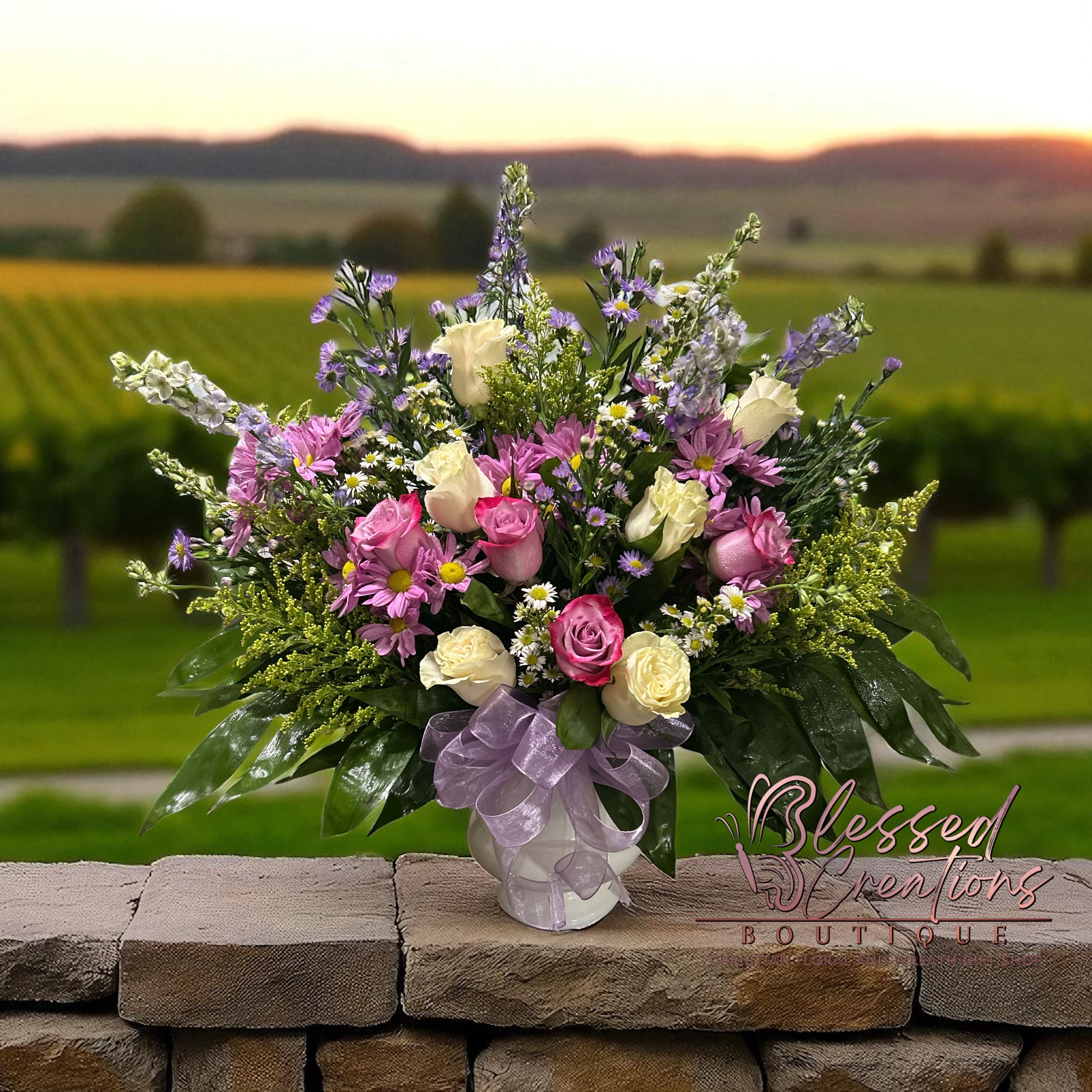 Heavenly Harmony  - Our Graceful Radiance Bouquet is a breathtaking mix of elegance and charm, perfect for celebrating life’s special moments. Designed with soft ivory roses, delicate pink roses, cheerful lavender daisies, and accents of lush greenery, this arrangement is finished with a sheer lavender bow for an extra touch of grace. Whether you’re sending encouragement, celebrating a birthday, or expressing sympathy, this bouquet makes a lasting impression. Hand-crafted with love at Blessed Creations Boutique in Valdosta, GA, we offer same-day delivery to local homes, businesses, hospitals, and funeral homes.