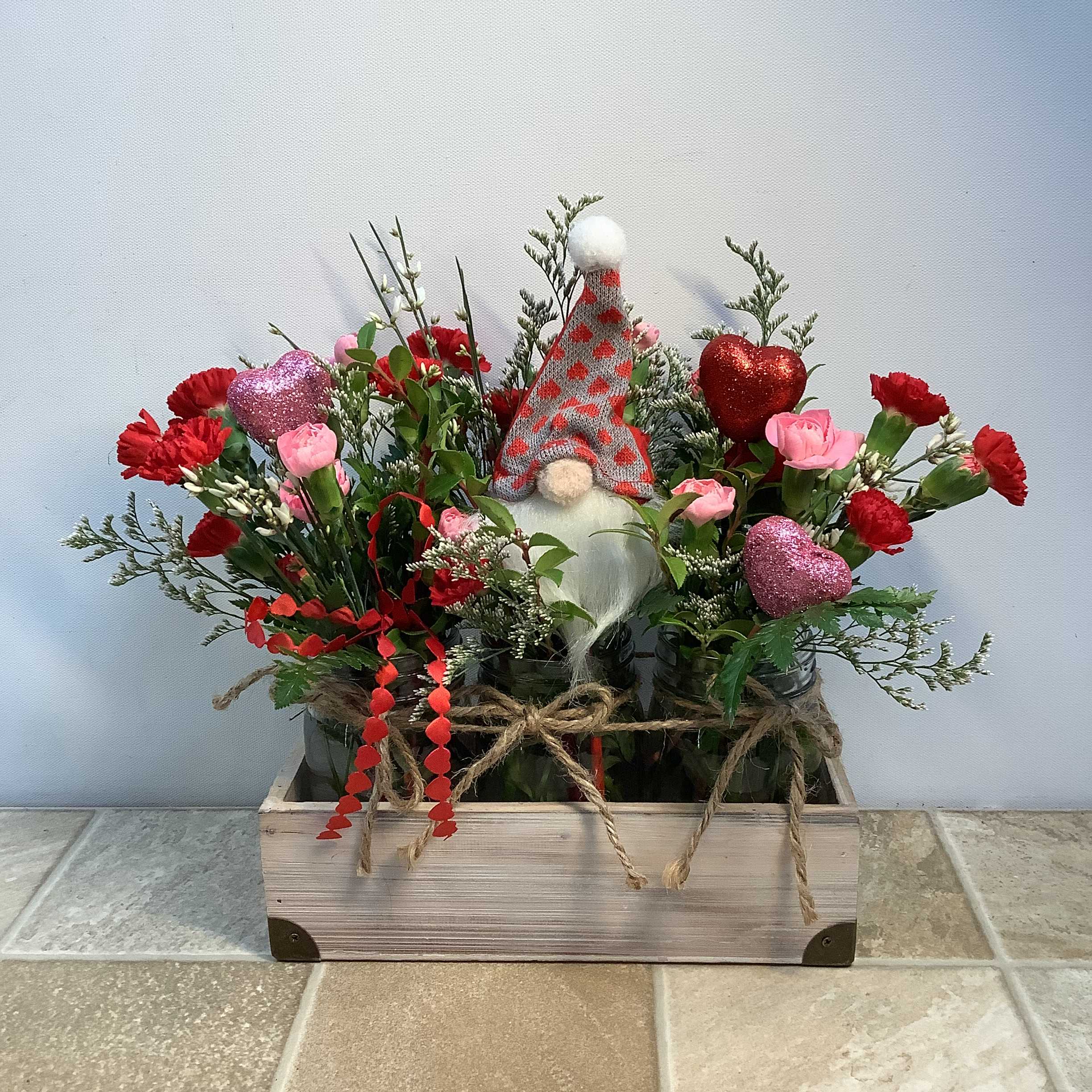 Meant For You - A charming arrangement in a 3 jar crate that’s “Meant For You”. It’s filled with long lasting pink and red mini carnations, glittered hearts and a fabric gnome. It measures 14” wide x 12” tall.