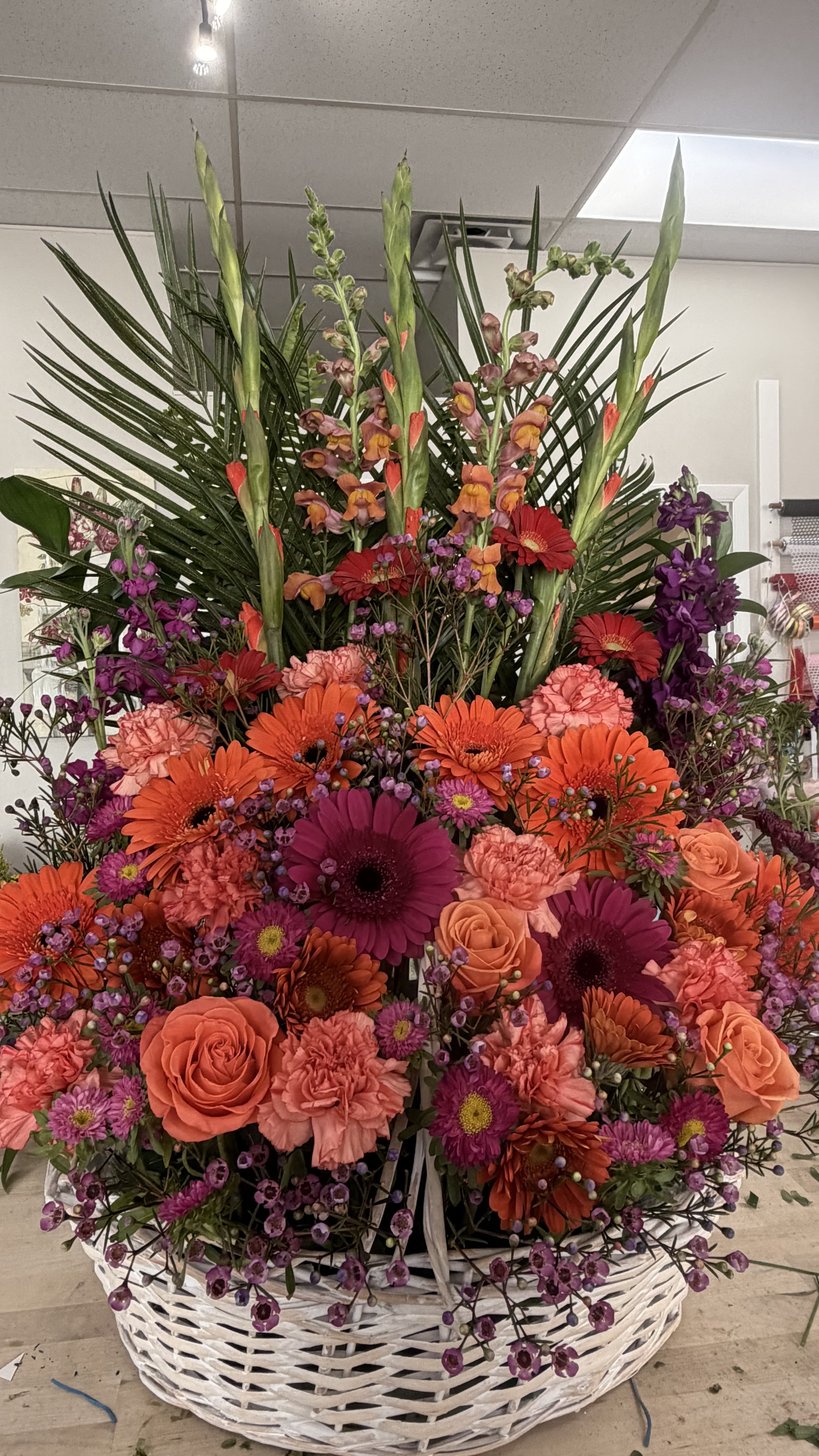 Sunset Splendor - A stunning and abundant basket arrangement featuring roses, gerbera daisies, carnations, snapdragons, and seasonal blooms in rich shades of orange, coral, purple, and pink. Accented with lush greenery and soft filler flowers, this design radiates warmth, beauty, and heartfelt expression.