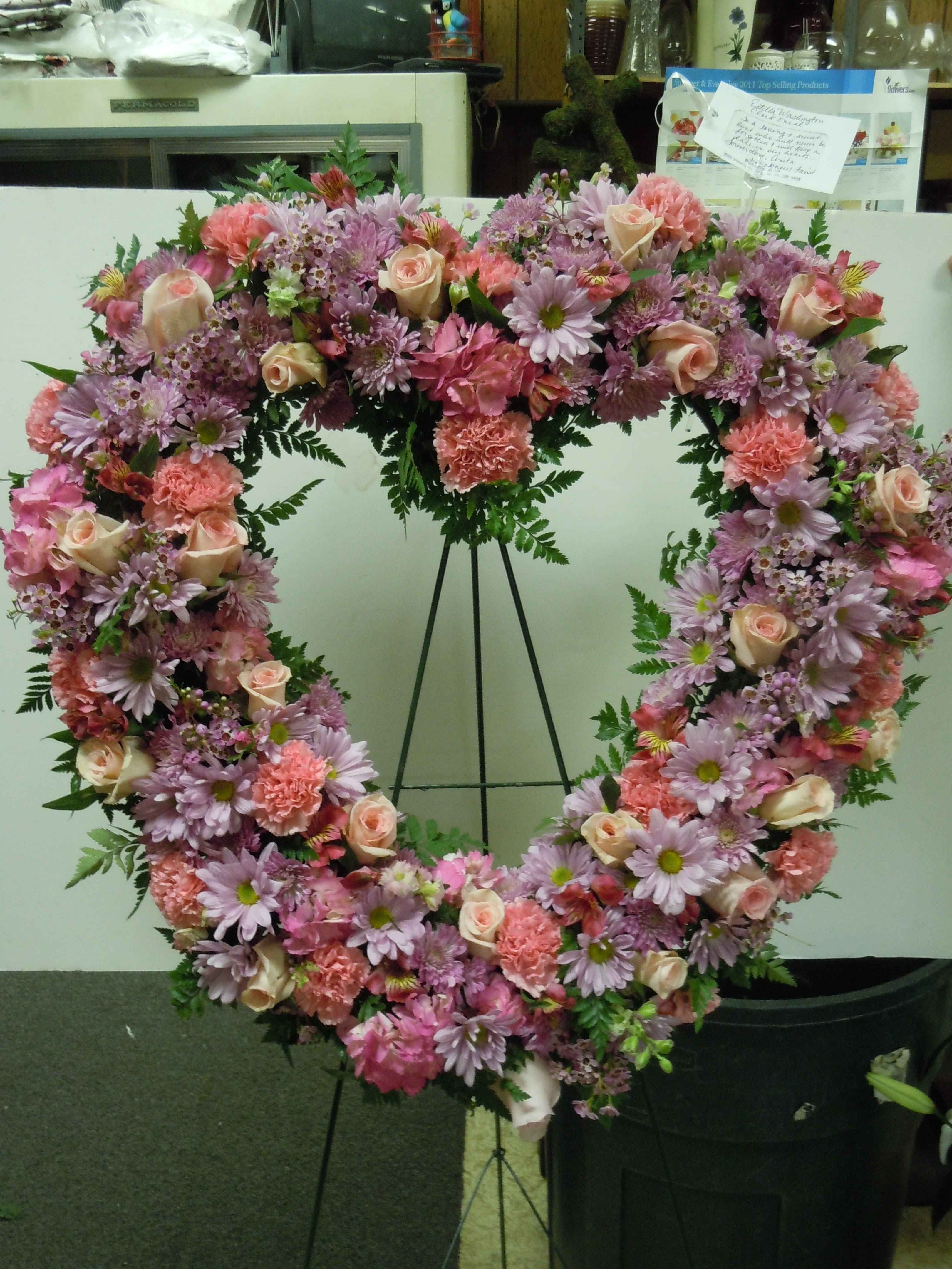 SP5 Standing Spray - An open heart with a mixture of lavender daisies, pink carnations, pink roses, lavender wax flower, pink alstromaria, baby's breath, greens  Banner - $15.00 + extra  Substitutions may apply due to flower availability