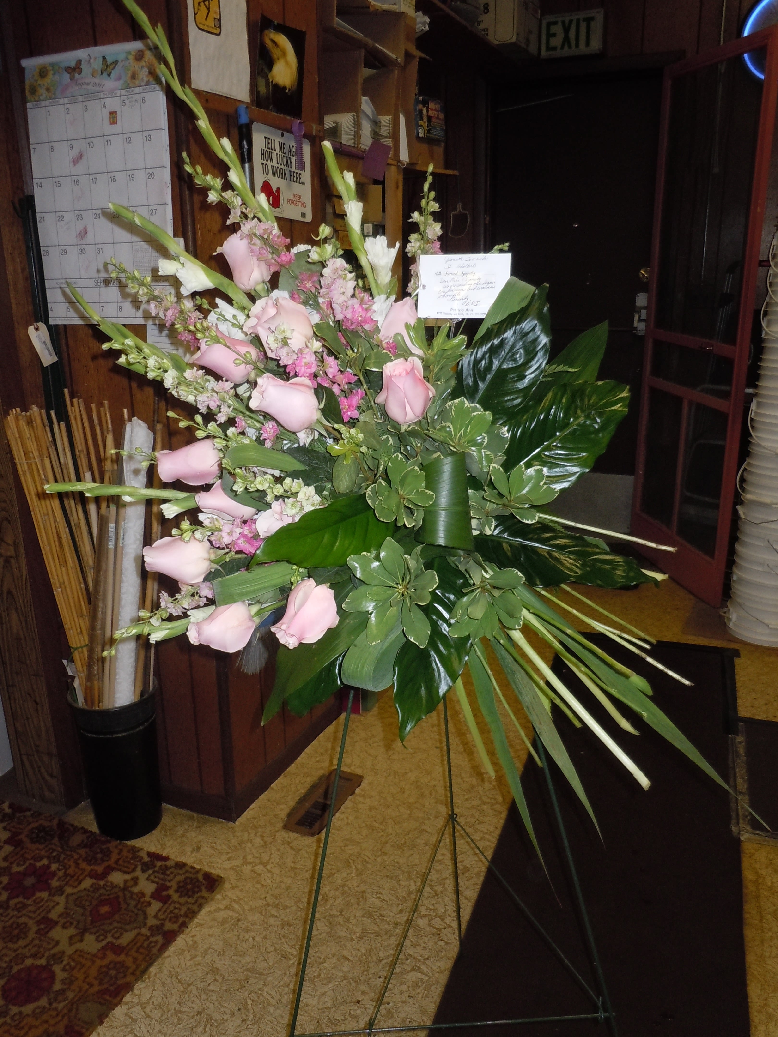 SP9 Standing Spray - A mixture of Pink gladiolas or pink larkspur, pink roses, tea leaves,  greens (colors can be changed)  Banner - $15.00 + extra  Substitutions may apply due to flower availability