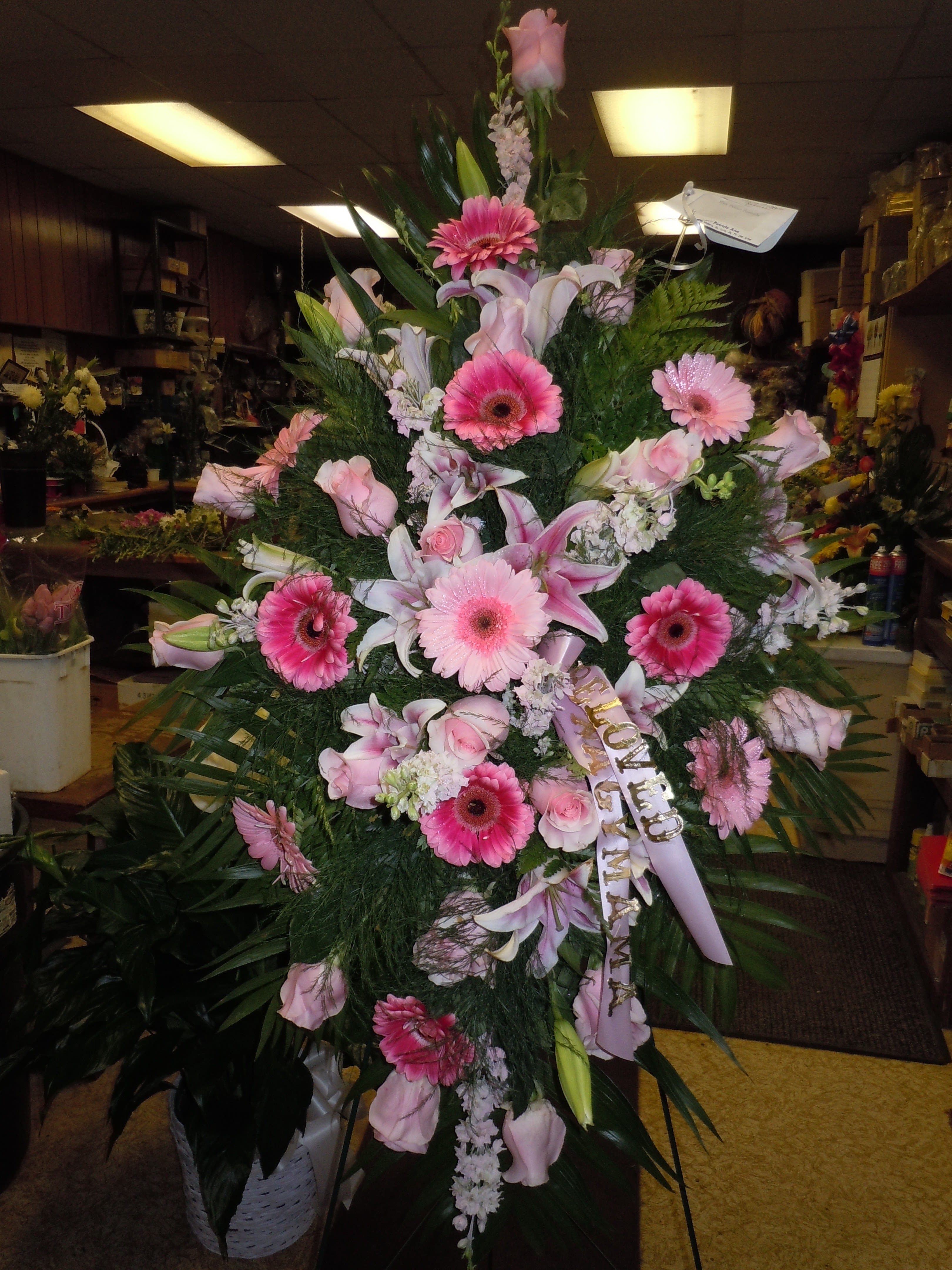 SP10 Standing Spray - A mixture of hot pink and light pink gerbera daisies, pink larkspur, pink roses, stargazer lilies, blue mist tinted pink, greens (colors can be changed)   Banner - $15.00 + extra   Substitutions may apply due to flower availability
