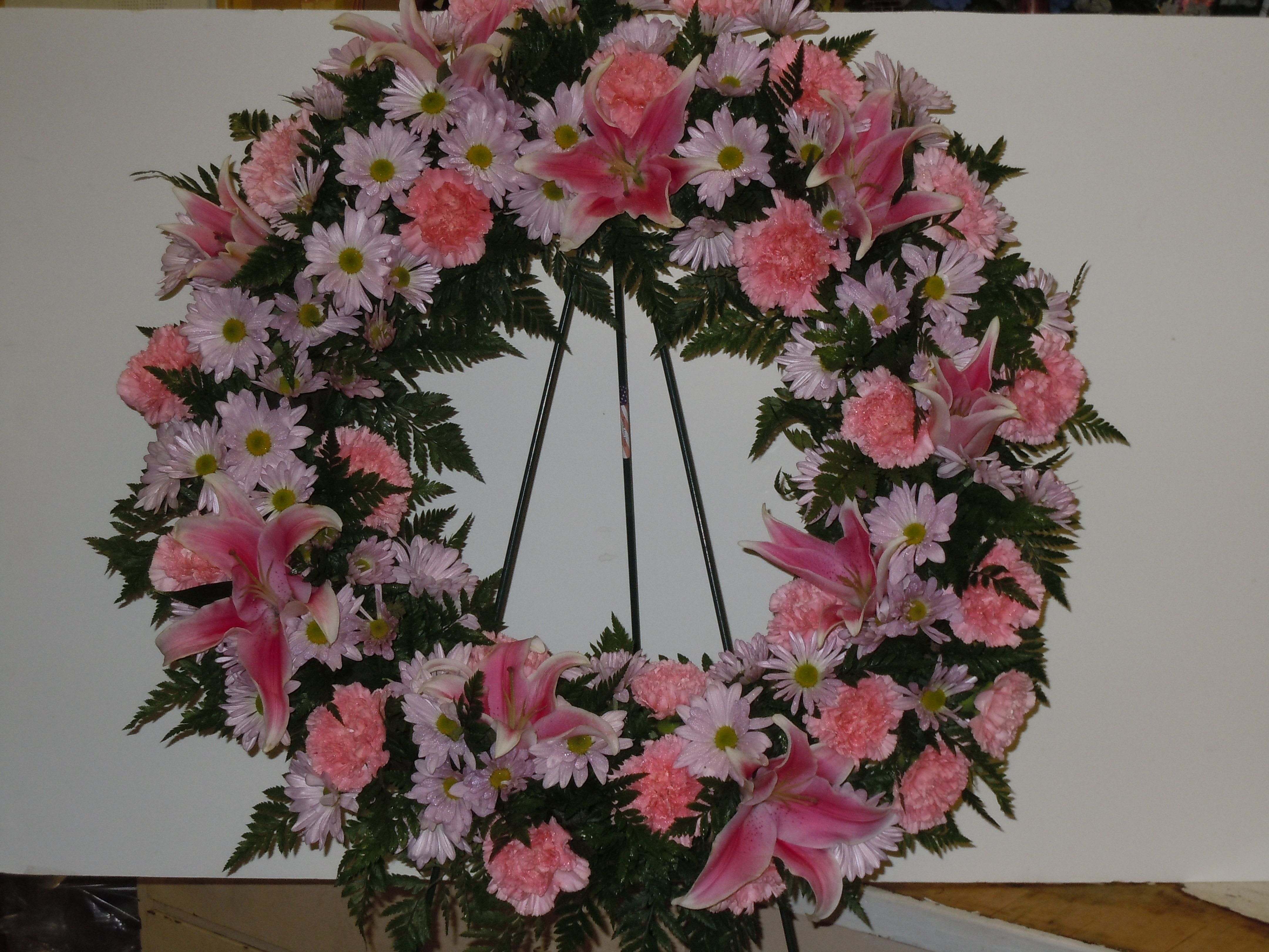 SP11 Standing Spray - An open wreath with a mixture of lavender daisies, pink carnations, stargazer lilies, greens   Banner - $15.00 + extra  Substitutions may apply due to flower availability