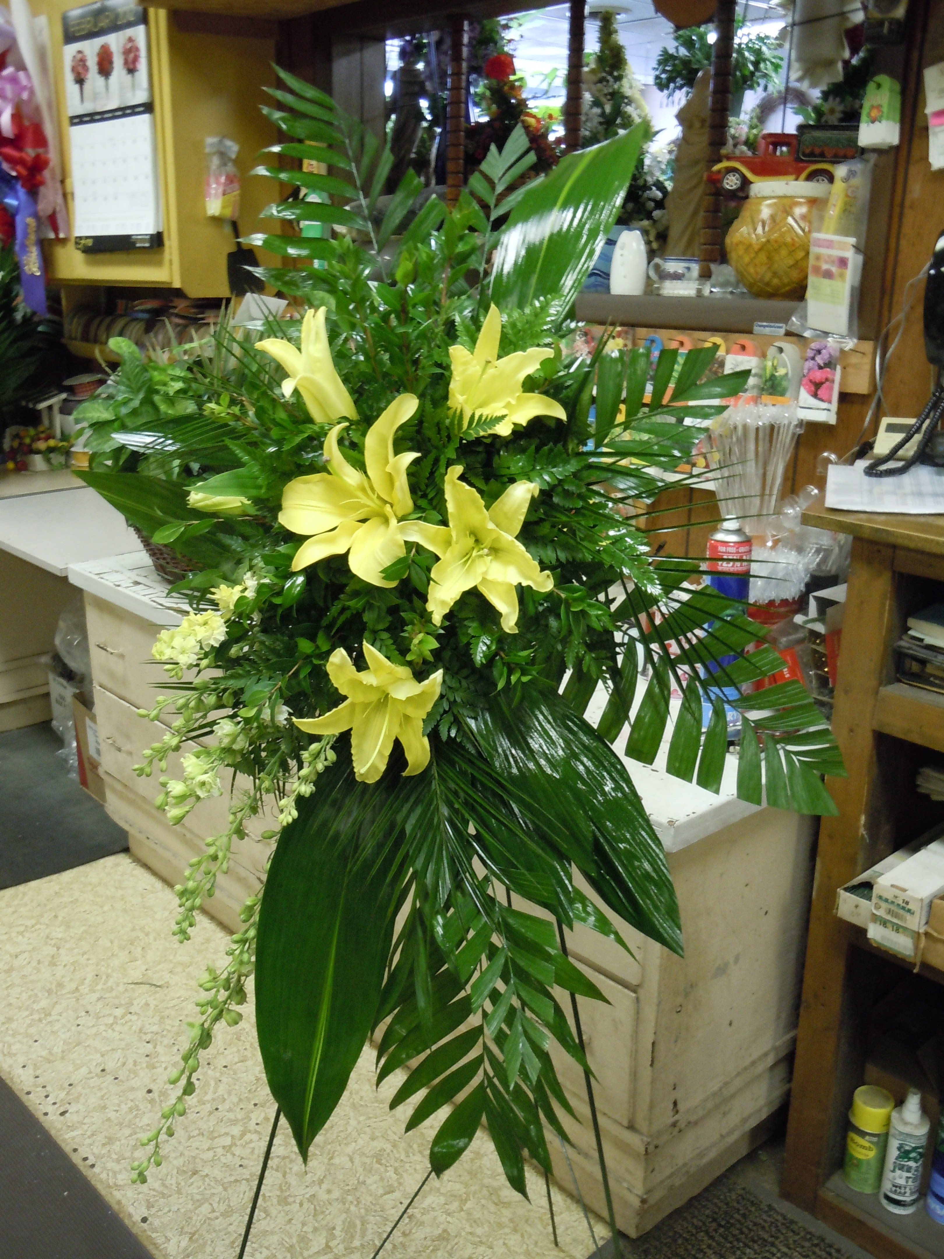 SP17 Standing Spray - A mix of white roses, red carnations, white lilies, Bells of Ireland, white snap dragons, baby's breath, tea leaves and greens.  Banner - $15.00 + extra  Substitutions may apply due to flower availability