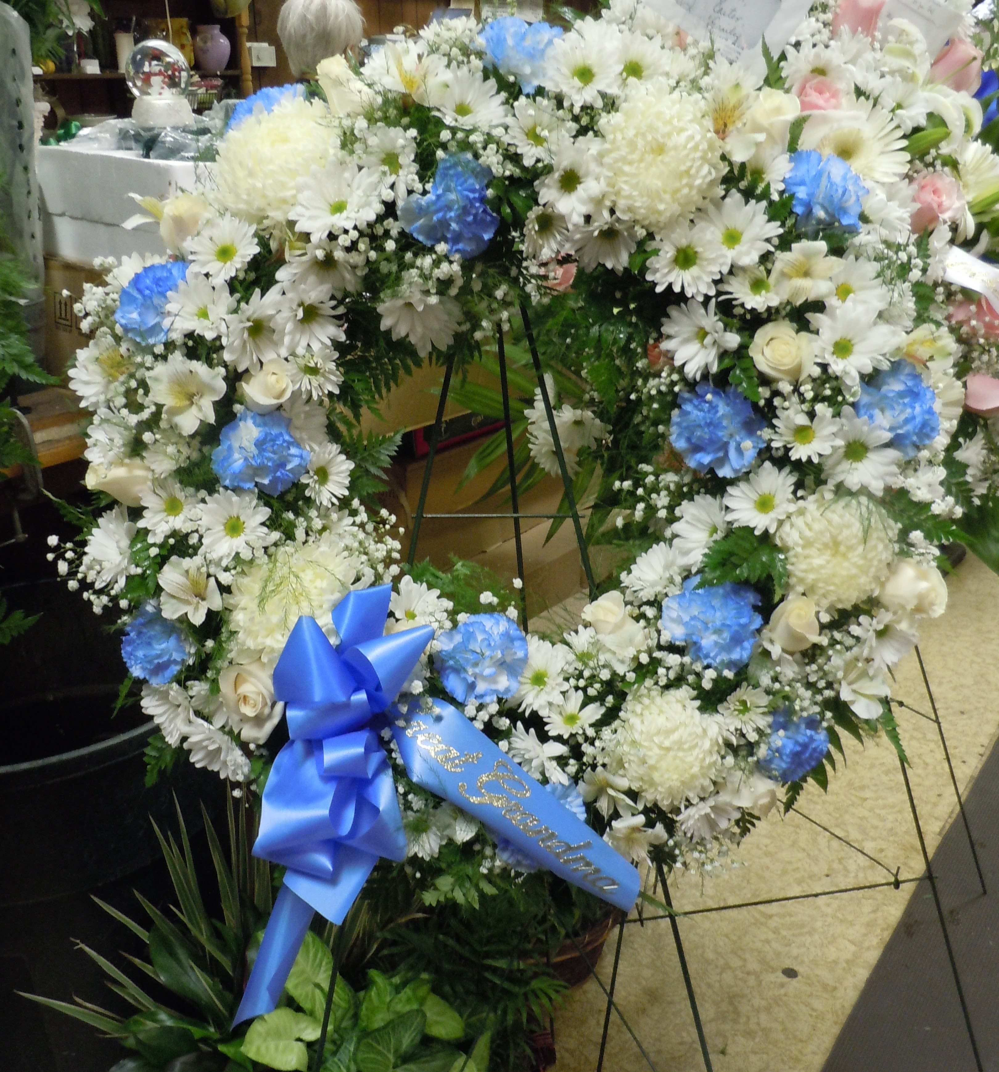 SP19 Standing Spray - A an open wreath with a mixture of fuji mums, carnations, roses, daisies, alstromaria, baby's breath and greens.  Banner - $15.00 + extra  Substitutions may apply due to flower availability