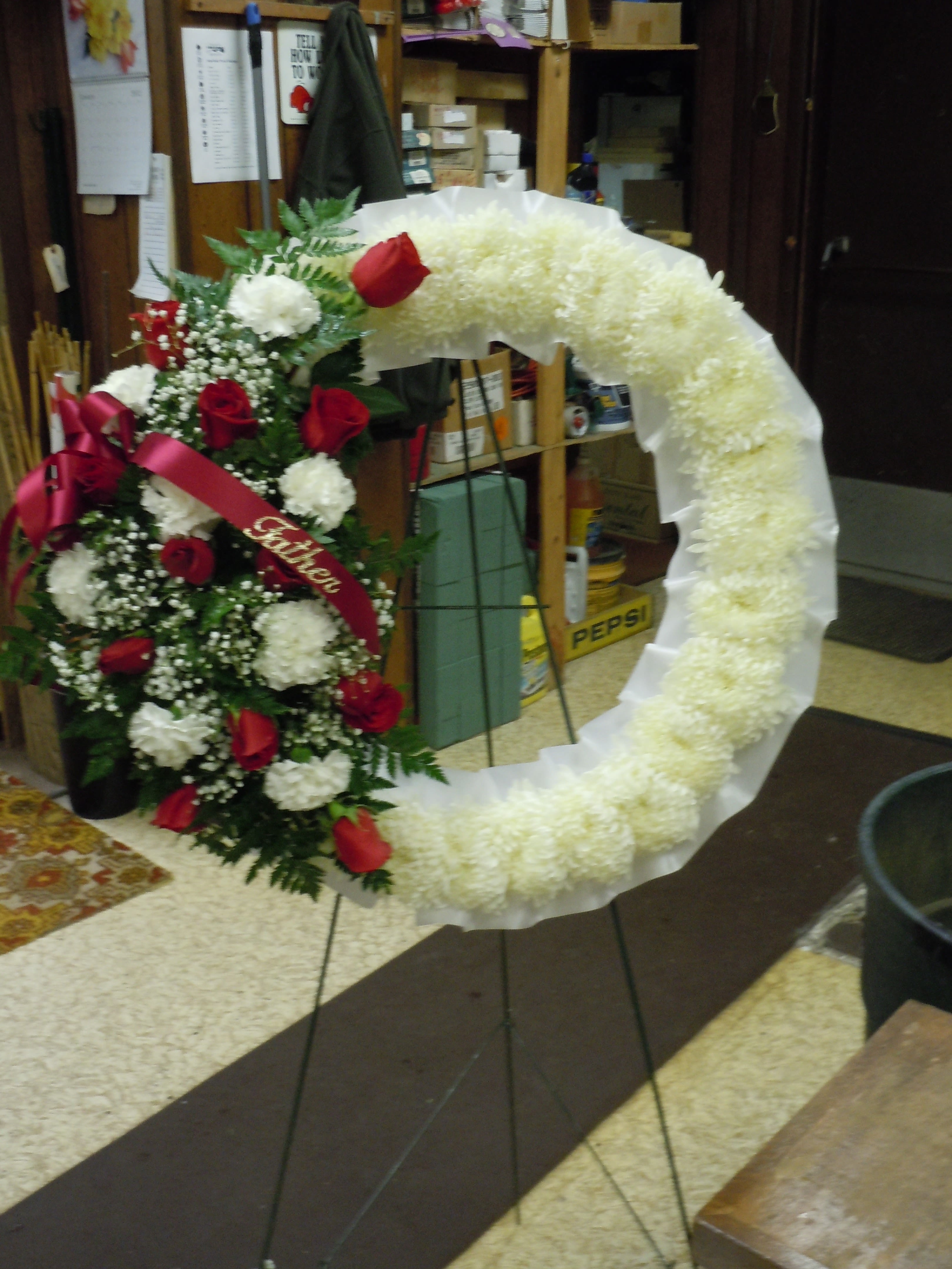 SP29 Standing Spray - An open wreath with a mixture of white fuji mums, red roses, white carnations, baby's breath and  greens.    Banner - $15.00 + extra  Substitutions may apply due to flower availability