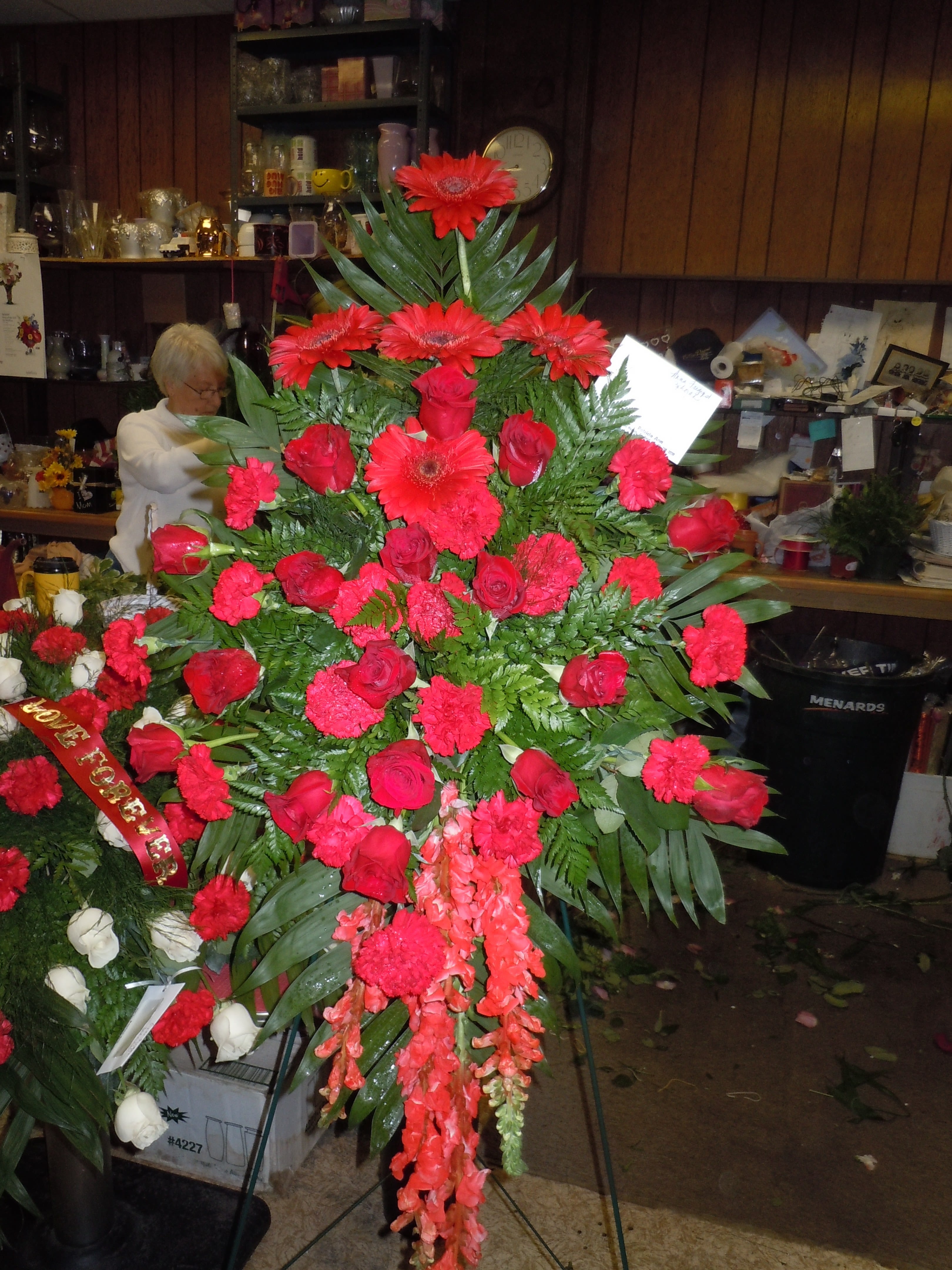 SSP31 Standing Spray - A mixture of red gerbera daisies, red roses, red carnations,  red snap dragons and greens.   Banner - $15.00 + extra   Substitutions may apply due to flower availability