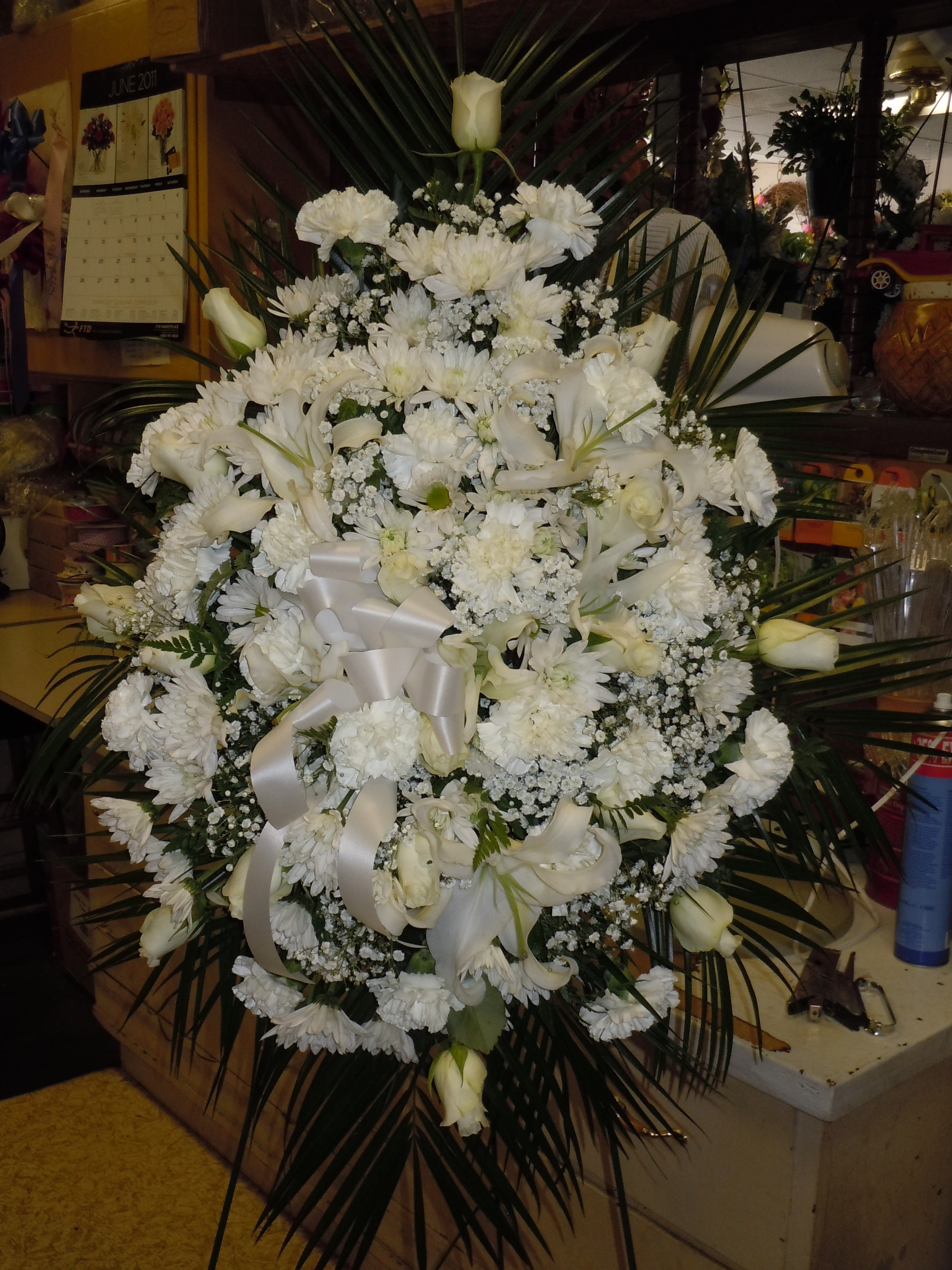 SP34 Standing Spray - A mixture of white carnations, white roses, white cushion mums, white lilies, baby's breath and greens.  Banner - $15.00 + extra  Substitutions may apply due to flower availability