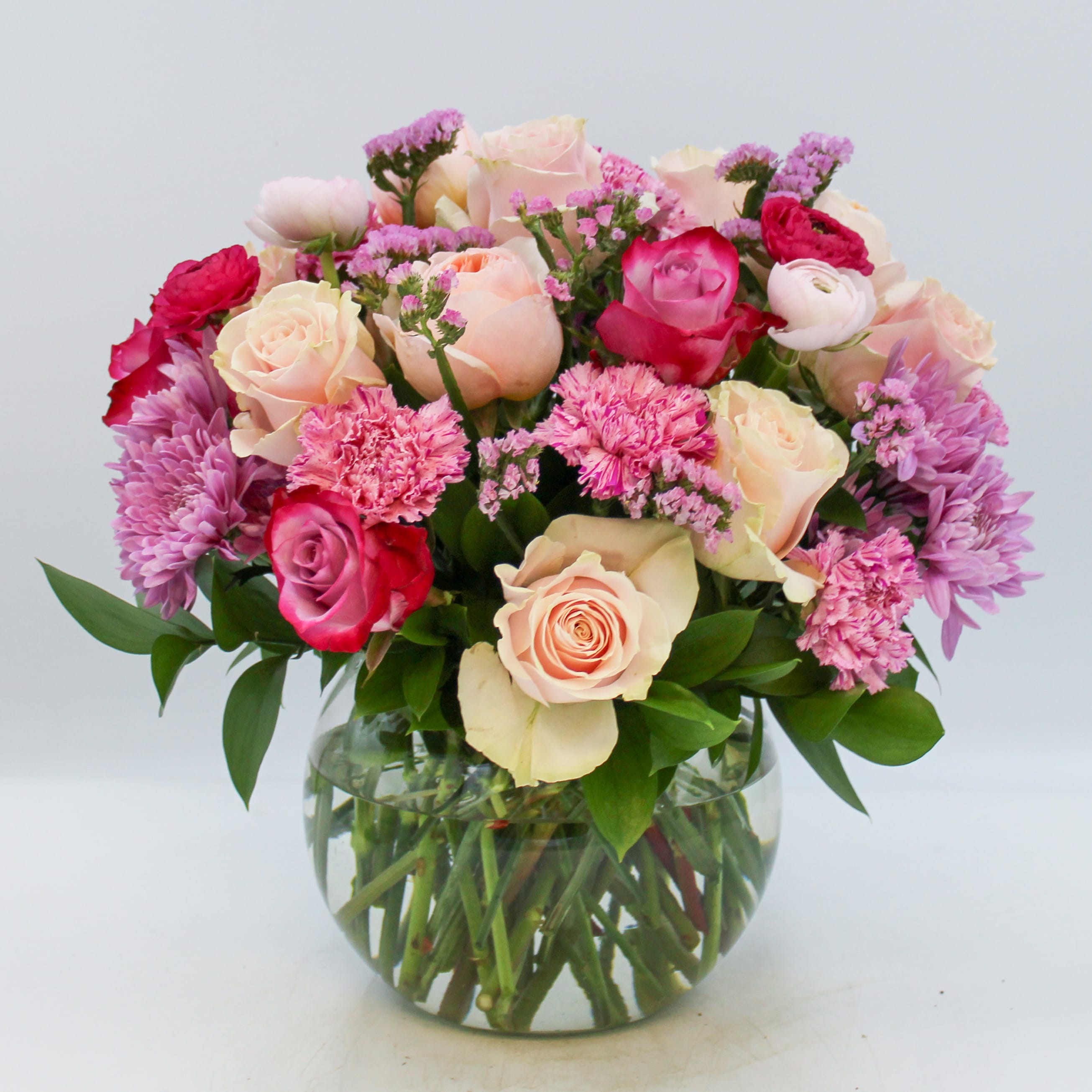 Romantique - Romantique is a luxurious and beautiful variety of blush and lavender florals that includes Roses, Ranunculus, Garden Roses, Pom Pom Mums, Statice, and Carnations in a bed of mixed seasonal foliage. Romantique is approximately 15 inches in height and 13 inches wide.