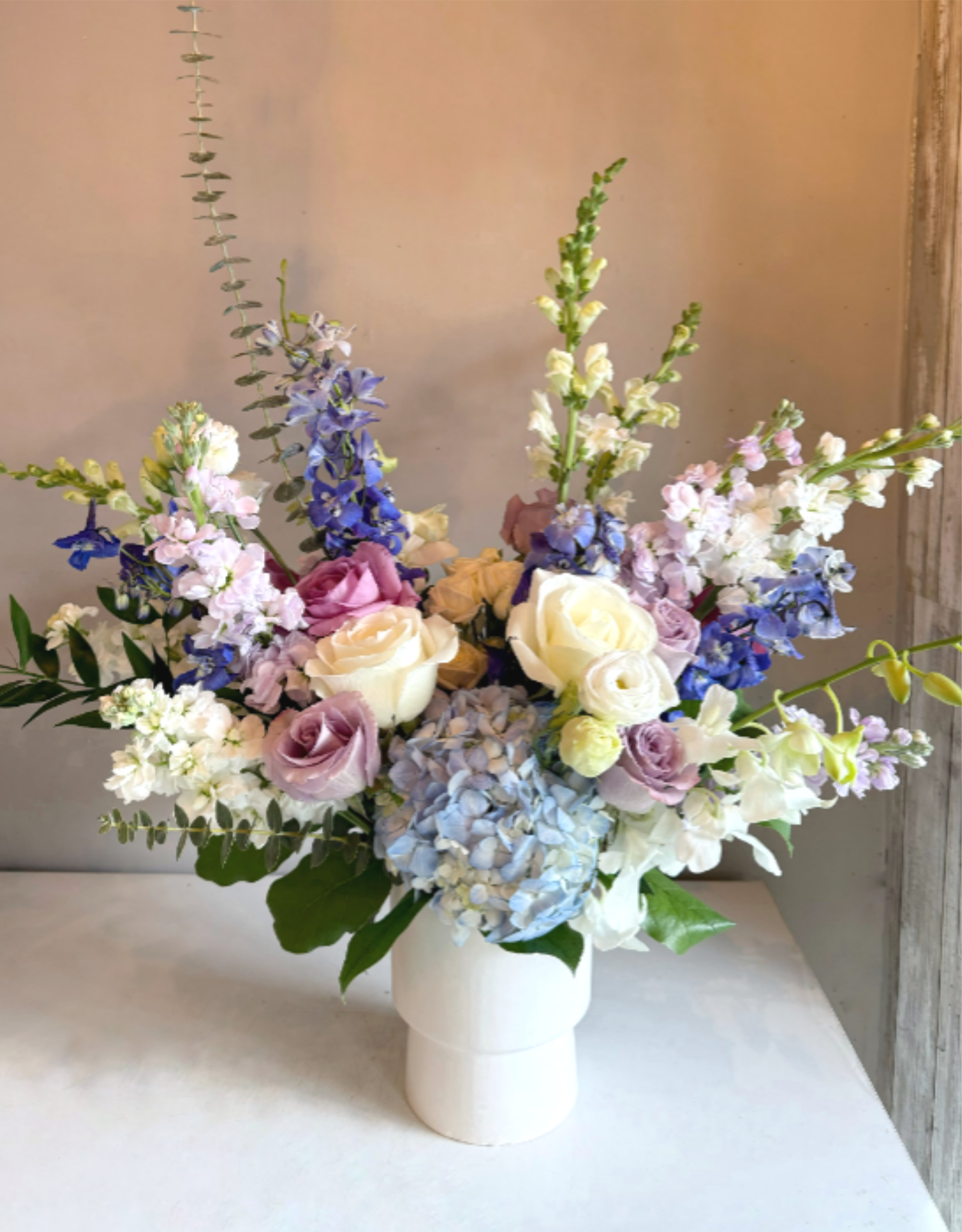 Celeste - This asymmetric arrangement exudes timeless elegance with a refined palette of blue, white, and lavender blooms. Carefully composed for a modern yet graceful look, it creates a sophisticated centerpiece perfect for any occasion. 