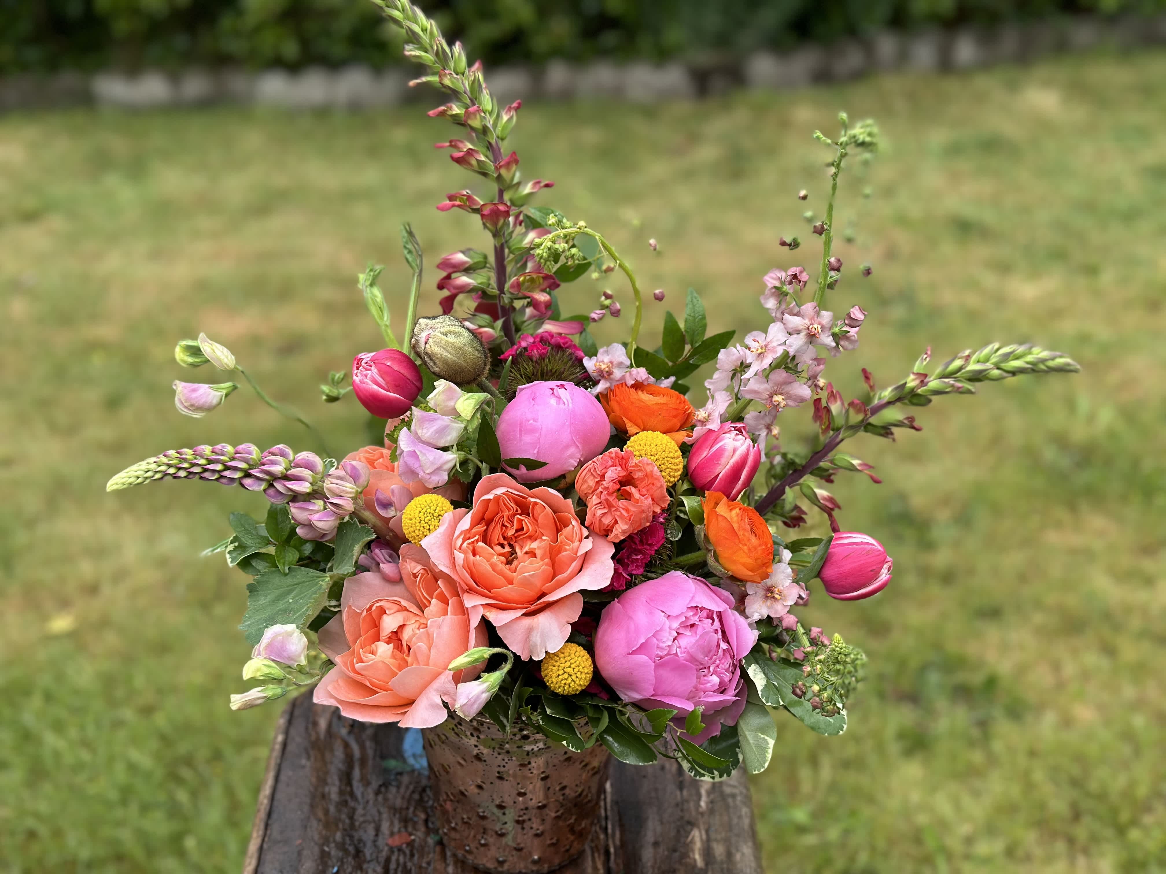 Chasing Sunsets Low and Lush - A Colorful arrangement in Sunset Hues of Pinks, Oranges, and Yellows using seasonal Blossoms.  *Please note that flowers included are an example of design. We will choose the finest blooms in this color palette.