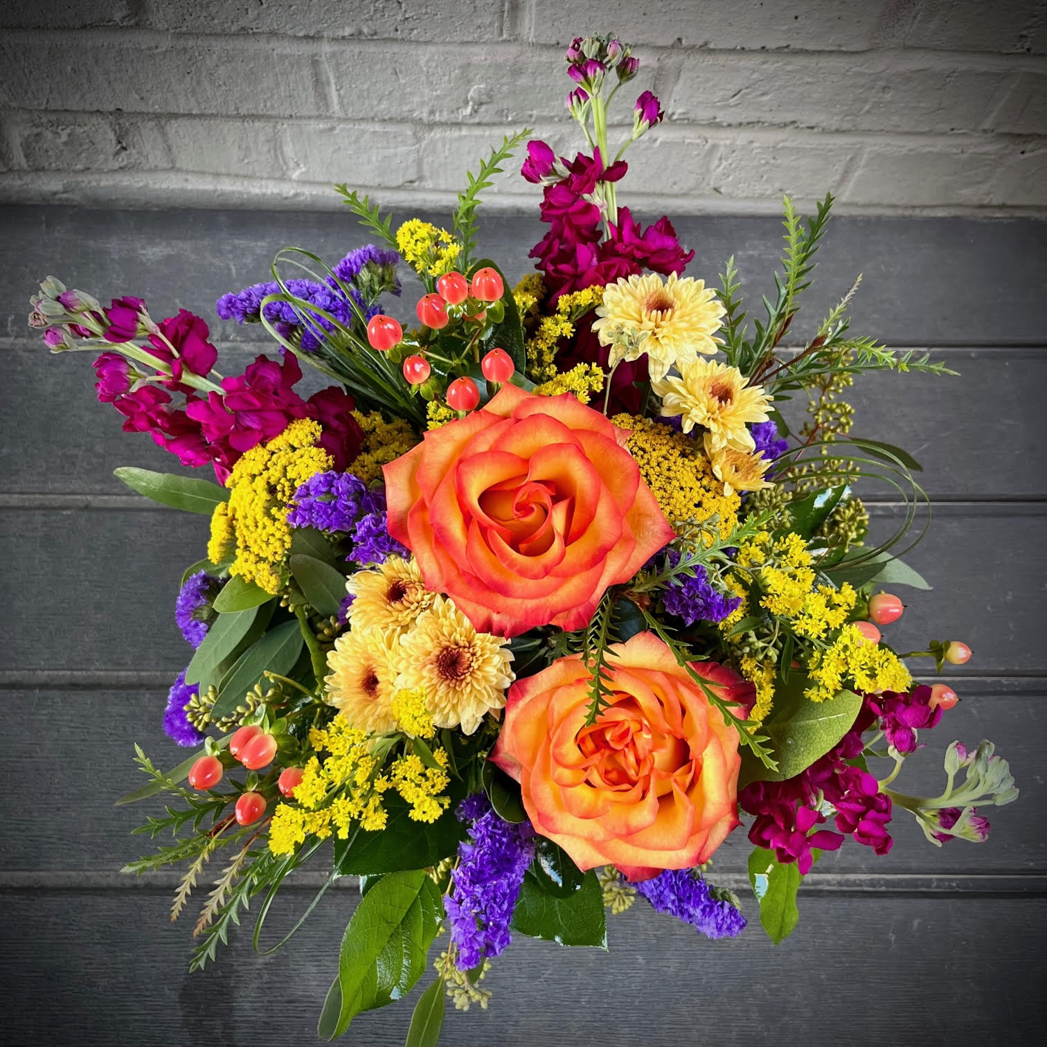 Tuscan Sunset - The Tuscan Sunset is a burst of bright colors: orange roses, fall mums, fuscia stock, purple status, and pink berries. Enjoy a colorful sunset, no matter the time of day, with this beautiful arrangement! Perfect for any home or office space. Approximately 13in by 14in.