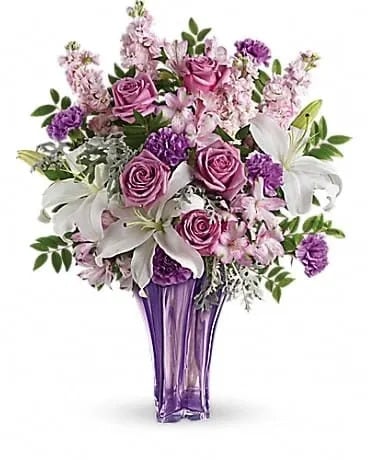 Lavished In Lilies Bouquet - Lush and lovely, this deluxe bouquet lavishes her with love! Pure white lilies shine amidst a marvelous mix of lavender roses and pink alstroemeria. Hand-delivered in a grand blown glass vase she'll treasure forever! Luxe lavender roses, white oriental lilies, light pink alstroemeria, lavender carnations and light pink stock are artistically arranged with huckleberry and dusty miller. Delivered in a Luxurious Lavender vase. 