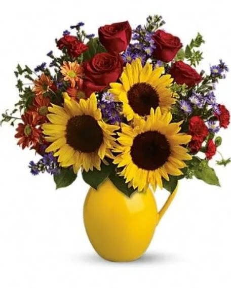 Sunny Day Pitcher of Joy - Symbolizing warmth and happiness, it is no wonder the sunflower is a quintessential ingredient in so many fall bouquets. This bouquet maximizes the joy of sunflowers by arranging them with a bevy of fall flowers, it's a lovely pick-me-up for a crisp fall day. Sunny sunflowers, red roses and miniature carnations, bronze daisy spray chrysanthemums, large lavender monte cassino asters and autumn greens are beautifully arranged in a ceramic vase. 