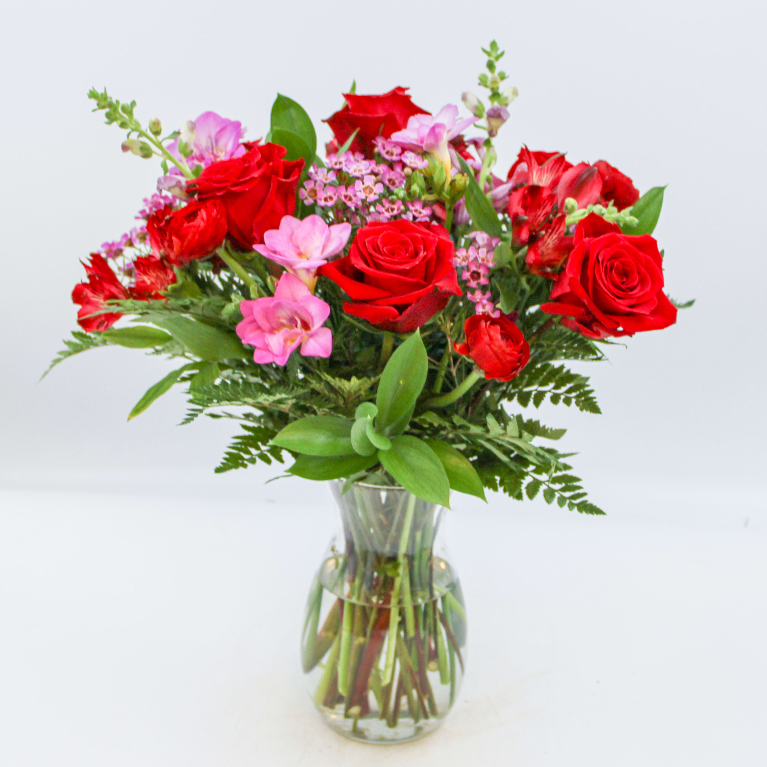 Oui - Oui is a classic beauty that includes Red Roses, Red Ranunculus, Red Alstromeria, Purple Freesia, Purple Waxflower and mixed seasonal foliage. Oui is designed in a clear glass Jordan vase, the Standard and Deluxe Sizes are approximately 16 inches wide and 17 inches tall. The Premium size is approximately inches 16 wide and 19 inches tall. 