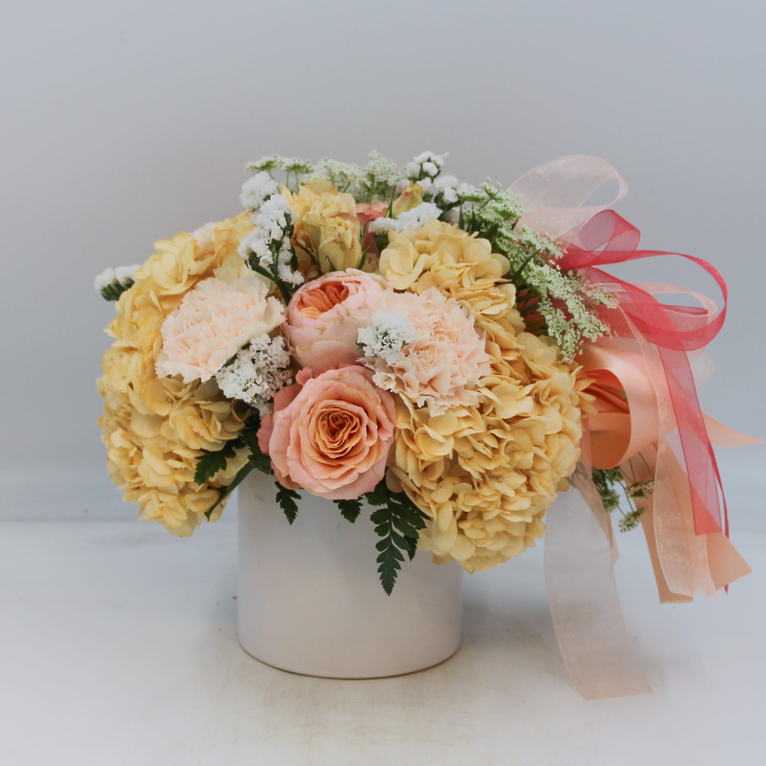 Paris - Paris is a limited edition design for our Valentine’s en vogue collection and features tinted Peach Hydrangea, gorgeous David Austin Garden Roses called “Juliet”, Shimmer Roses, Peach Spray Roses, Peach Carnations, White Statice and Queen Anne’s Lace arranged in a white keepsake ceramic pot adorned with Peach, Champagne, Coral and Ivory satin and chiffon ribbons. 