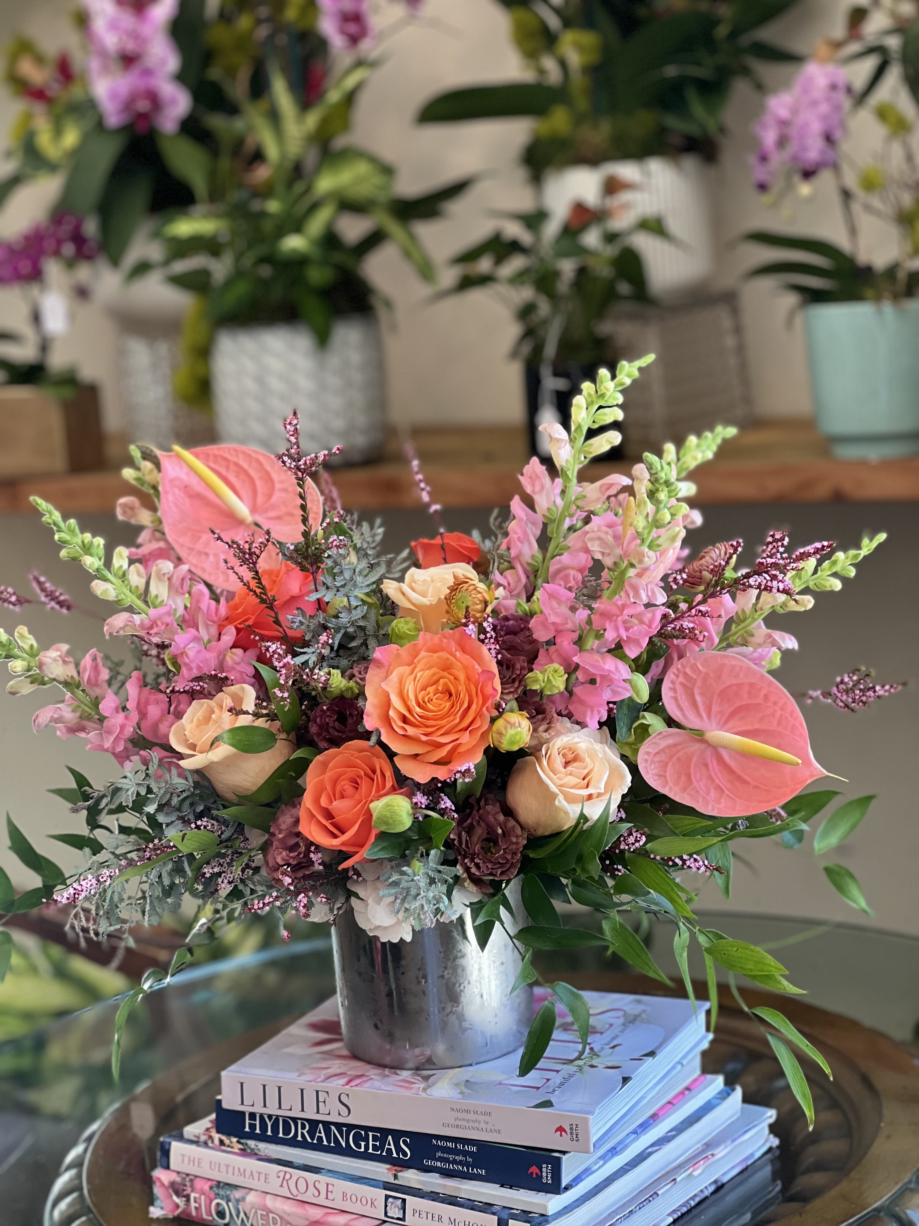 Cleo Sol  - Our "Cleo Sol" arrangement is a refreshing way to celebrate bright sunny days. This arrangement captures the essence of the sun in an energetic and zesty way.   Florals included: Free Spirit roses, pink anthuriums, pink snapdragons, orange crush roses, mauve lisianthus, pink scottish heathers, italian ruscus, and acacia.  Designed in a silver 5x5 cylinder vase. This arrangement stands approximately 15" inches tall and 22" inches wide. 