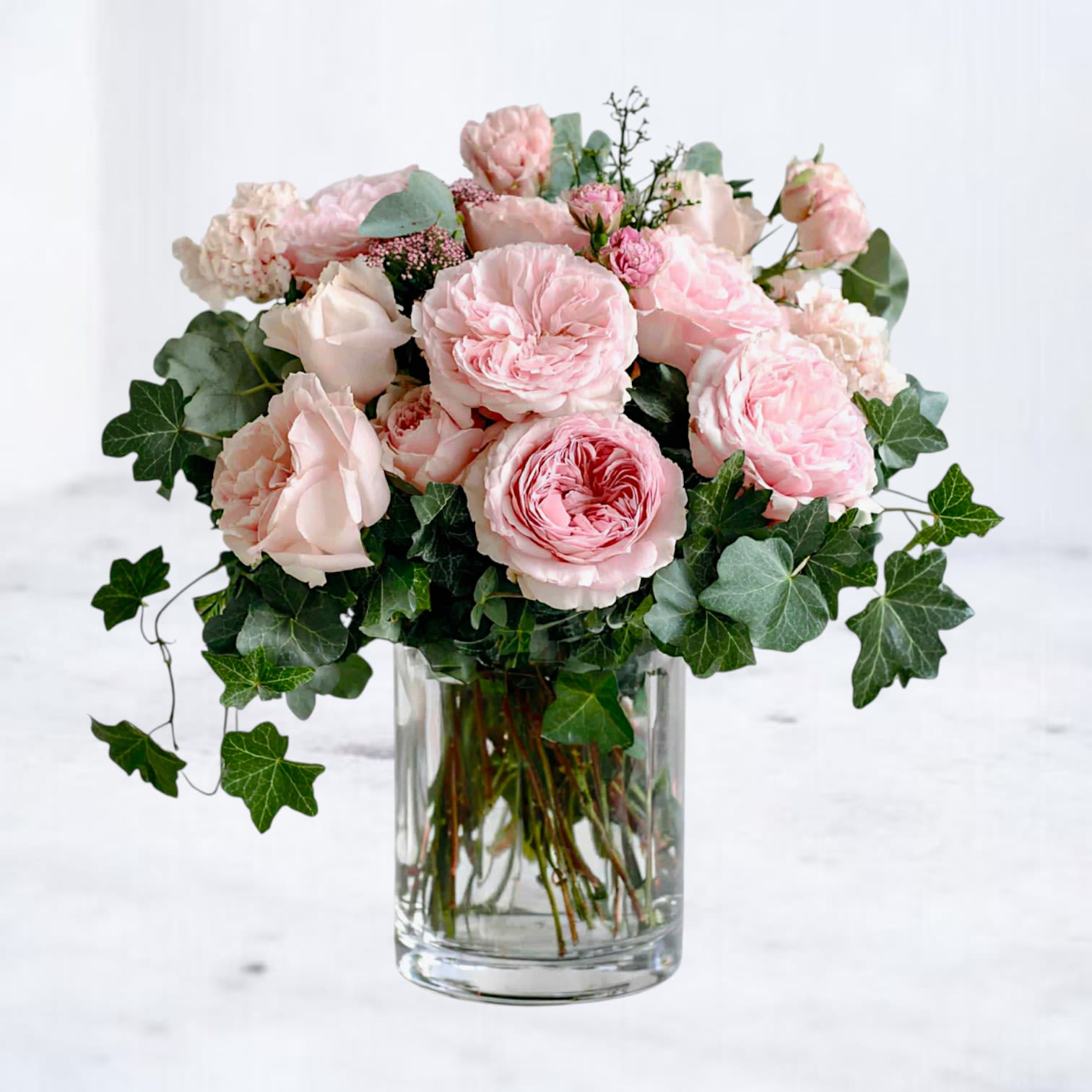 Aveline - Soft, romantic, and effortlessly refined, Aveline is a garden-inspired arrangement designed to speak the language of love—quietly and beautifully. 12 Blush garden roses take center stage, layered with delicate seasonal blooms and lush trailing greenery for a look that feels both intimate and natural.  Perfect for Valentine’s Day, anniversaries, or simply reminding someone they’re cherished, Aveline captures a gentler kind of romance—one rooted in warmth, connection, and timeless beauty.