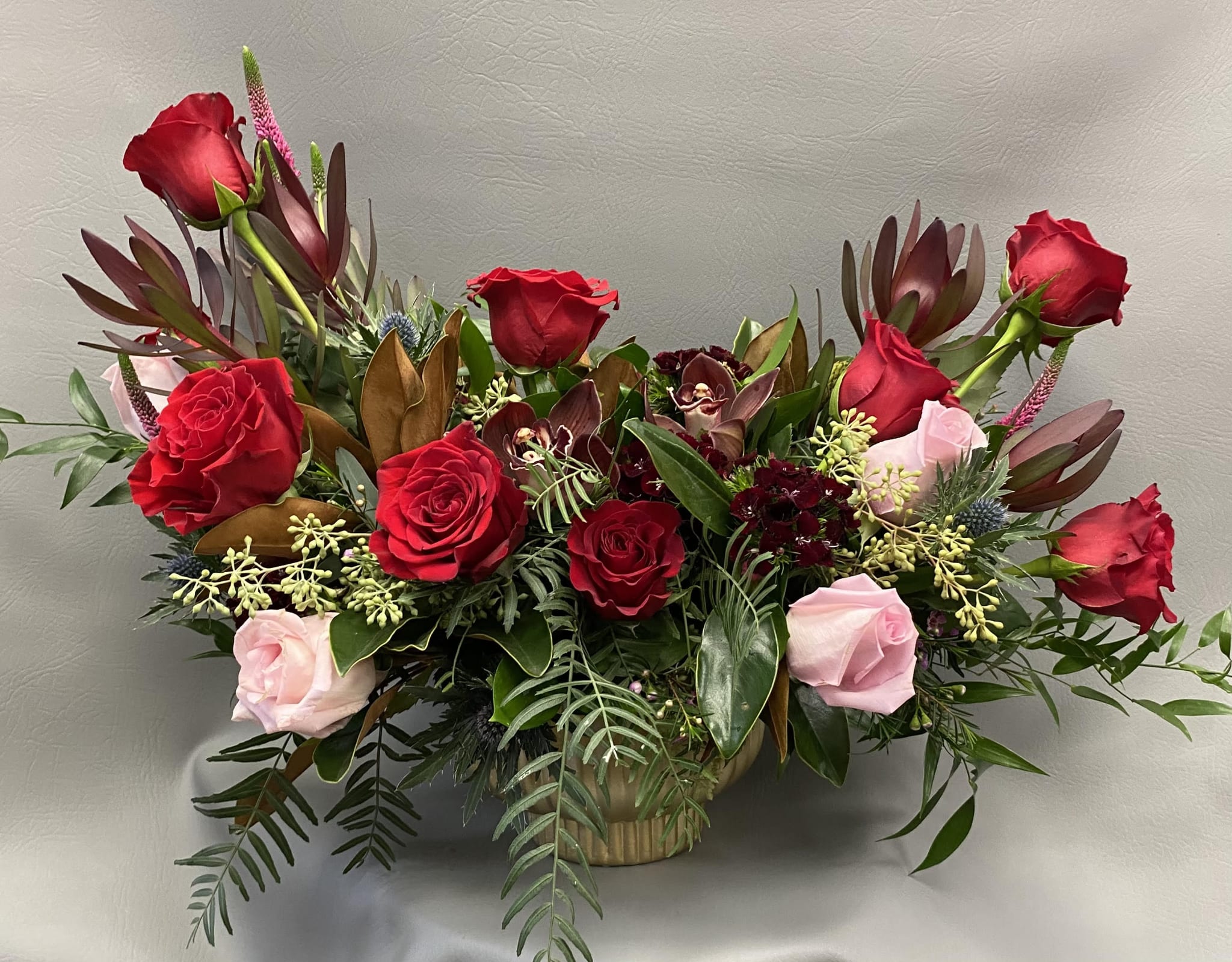 Passion and Grace - Deep red roses symbolize passion, while blush roses and delicate orchids add softness and elegance. Arranged with lush greenery in a low-profile container, Passion &amp; Grace is a sophisticated statement of love and devotion.