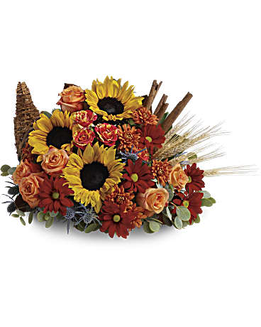 Classic Cornucopia - Celebrate the season of Thanksgiving with this traditional symbol of autumnal abundance. The perfect Thanksgiving table decoration, this beautiful cornucopia is rendered as a horn-shaped wicker basket filled with fall flowers and harvest wheat. Also, ideal for the kitchen counter, coffee table or entryway. Gorgeous sunflowers and lush orange roses are accented with unique blue eryngium, red daisies, yellow cushion mums, parvifolia eucalyptus and magnolia leaves in a wicker cornucopia-shaped basket. Cinnamon sticks and harvest wheat are comforting fall touches. Orientation: One-Sided