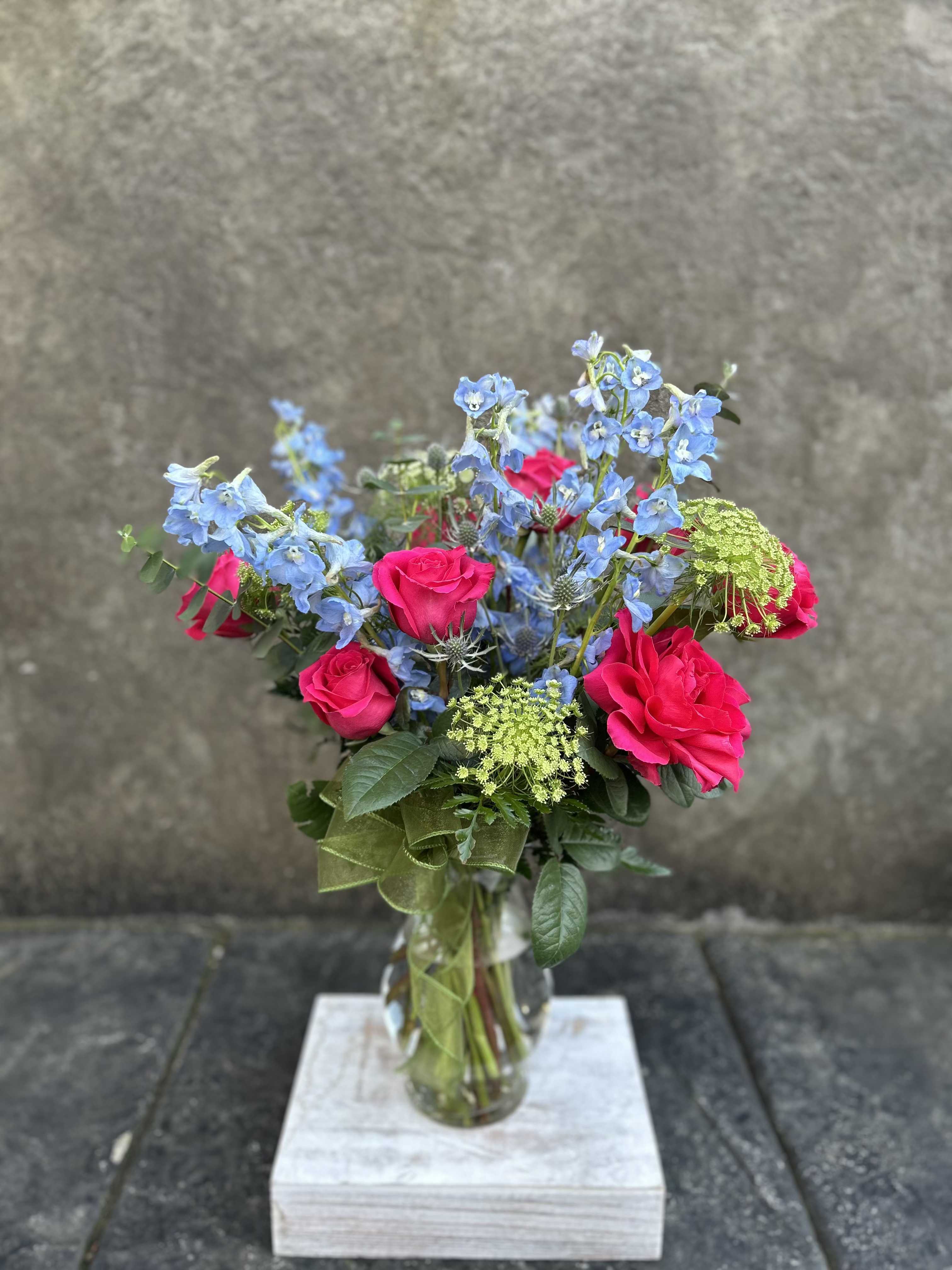 Bella  - Delphinium is the flower of the year, this design is meant to showcase their beauty.  Sky blue delphinium , hot pink roses, queen lace, eryngium, and eucalyptus with a decorative ribbon.   *Reasonable substitutions may be made due to floral availability. Will have same overall look and feel.