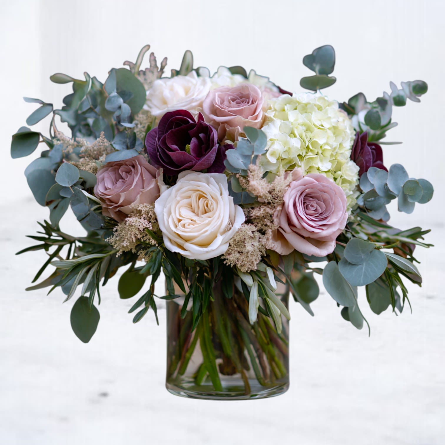 Serelle - Soft, refined, and quietly romantic, Serelle blends café mauve and blush roses with creamy whites, fresh hydrangea, and layered eucalyptus for a look that feels both modern and timeless. A deep, velvety accent bloom adds depth and contrast—an understated nod to passion without overpowering the palette.  Designed with Valentine’s Day in mind but beautiful year-round, Serelle is perfect for anniversaries, meaningful gestures, or moments when words fall short. Its natural movement, muted tones, and lush greenery create an arrangement that feels intimate, intentional, and effortlessly elegant.  Arranged in a clear glass vase. Flower varieties may vary slightly based on seasonal availability, but the overall color palette, shape, and style will remain true to the design.