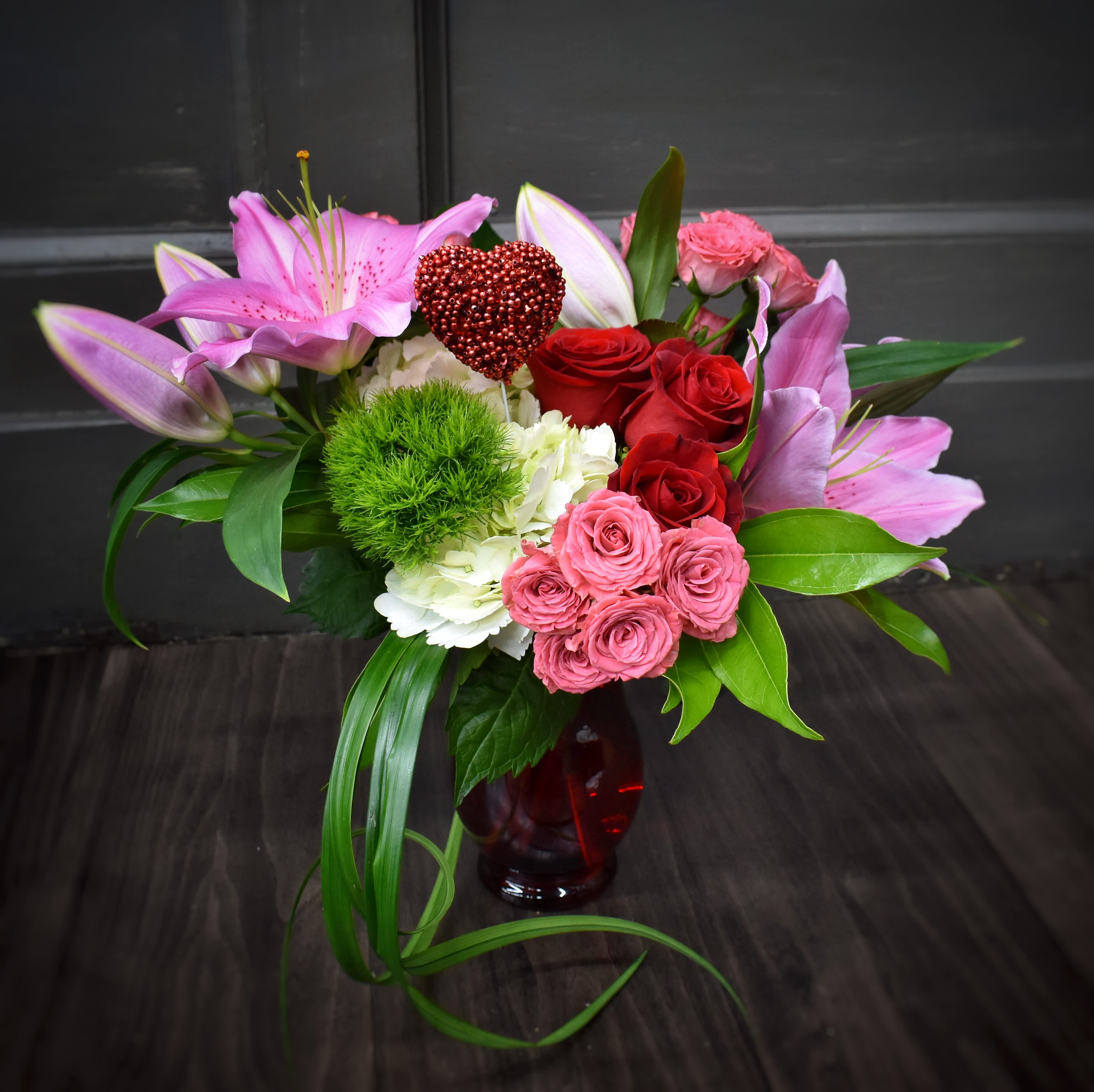Be Mine Pemium - A ruby red glass vase is filled with a fluffy white hydrangea and 3 red roses, fragrant lilies, 3 stems of spray roses, a green trick dianthus and accented with green foliages and a heart pick.