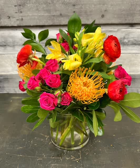Hot Lola - Hot Lola is small and packed full of personality with fierce red ranunculus, hot pink spray roses, yellow alstromeria, and orange protea.