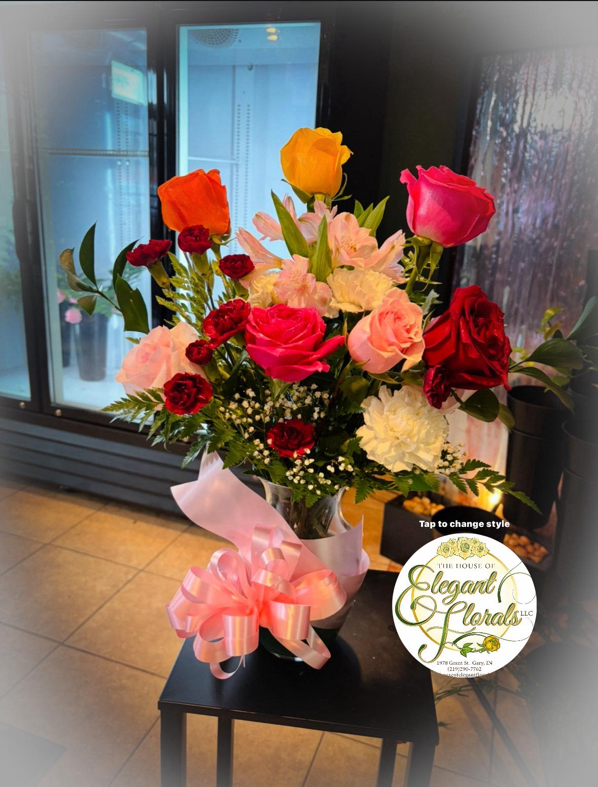 Radiant Garden Rose Vase Arrangement - This vibrant garden-style vase arrangement is a joyful mix of bold color and classic elegance. Featuring premium roses in rich red, hot pink, soft blush, sunny yellow, and warm orange tones, this design is beautifully complemented by delicate alstroemeria, mini carnations, white accent blooms, and lush seasonal greenery.  Arranged in a clear glass vase and finished with a soft pink ribbon, this eye-catching piece is perfect for birthdays, celebrations, thank-you gifts, or simply to brighten any room. Each arrangement is handcrafted by our florists using the freshest flowers available.