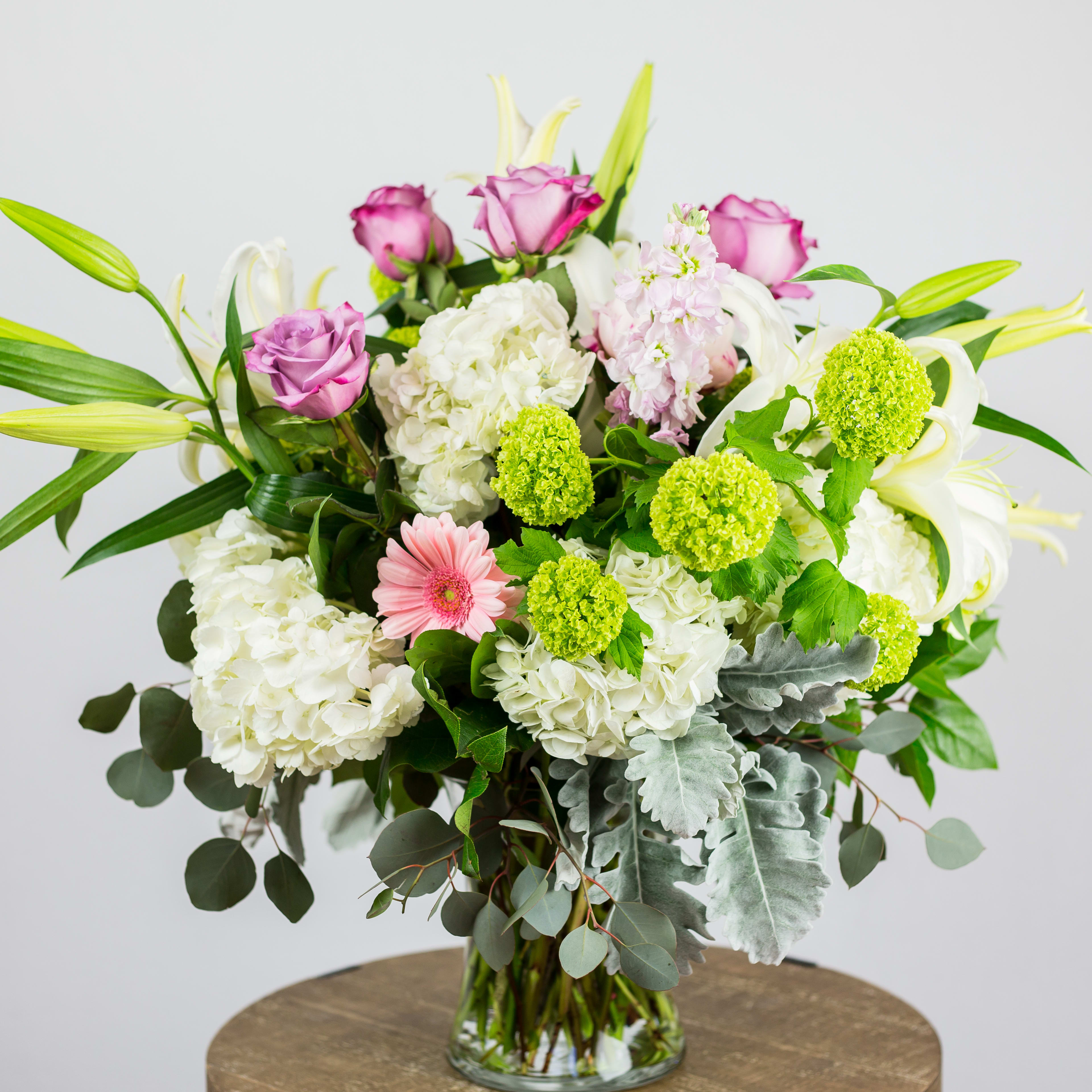 Heavenly - Oriental Lilies, Hydrangea, Dusty Miller, Gerbera Daisies, green Viburnum, Peonies, Purple Roses, Stock. Flowers and containers availability is depending on season and product market.
