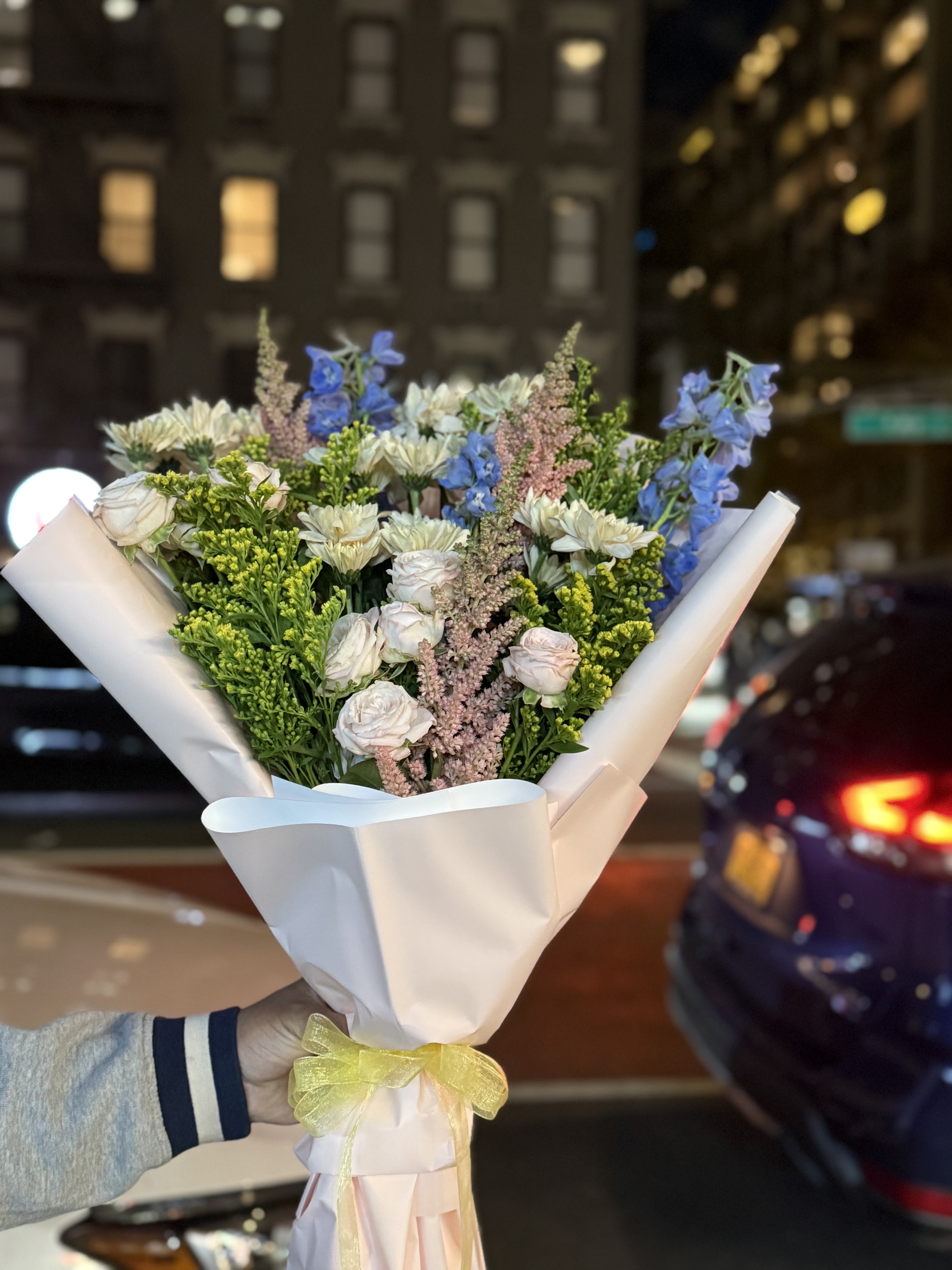 Mia’s Pastel Garden - Mia’s Pastel Garden Bouquet is a soft and romantic floral arrangement featuring delicate blush roses, creamy chrysanthemums, airy blue delphiniums, pastel pink astilbe, and fresh seasonal greenery. Thoughtfully wrapped in elegant paper and finished with a gentle ribbon, this bouquet brings a light, graceful charm perfect for birthdays, celebrations, or just because. Please note: this arrangement comes as a wrapped bouquet only and does not include a vase.