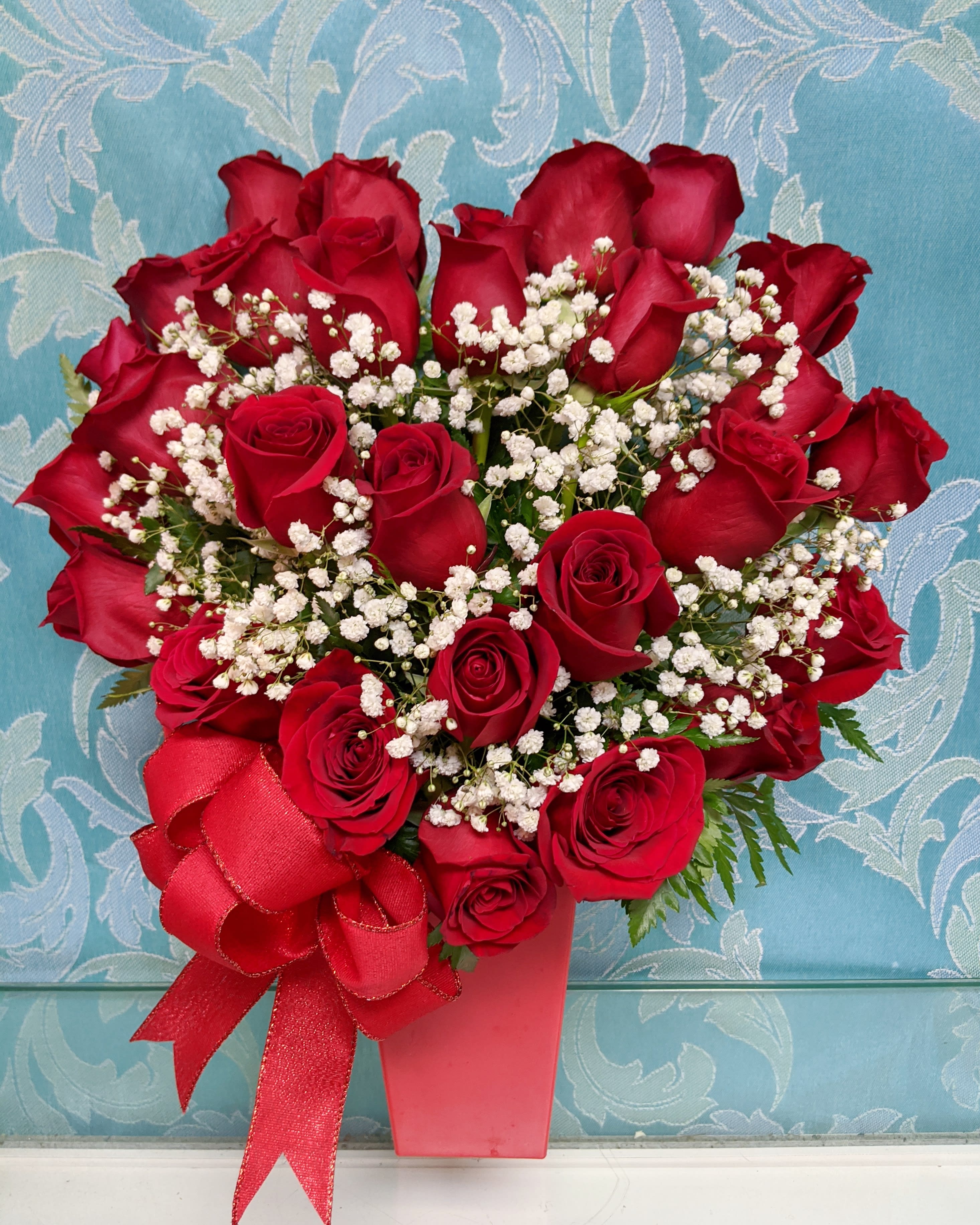 2 Dozen Heart Full Of Love - 2 Dozen red roses in a heart shape with babies breath and a tall red container with a red bow. 