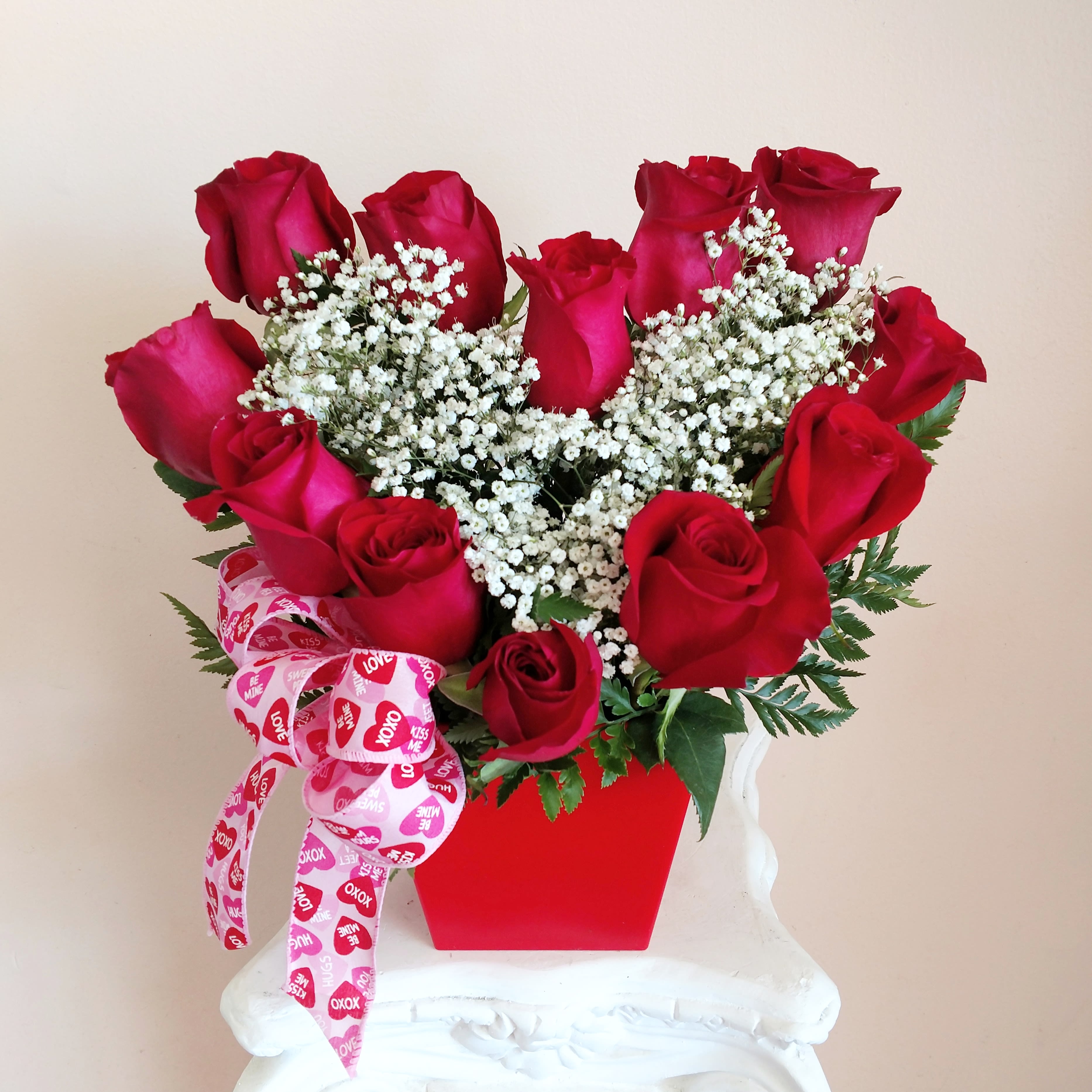 Be Still My Heart - Rose heart design with one dozen large bloomed Ecuadorian roses in a red or pink container and red bow.