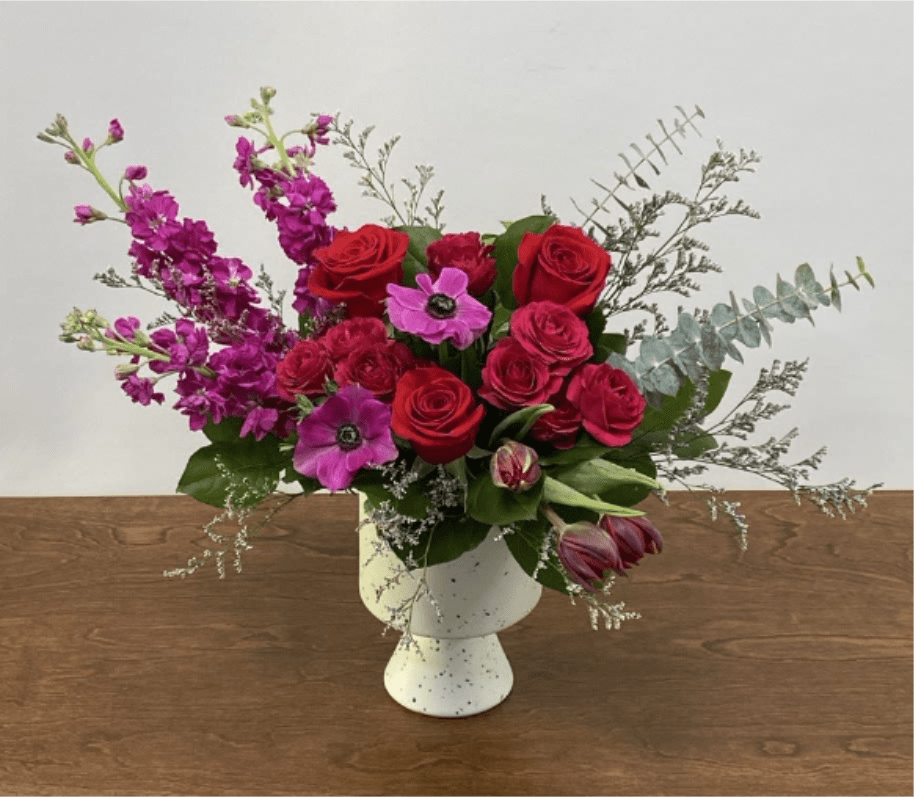 Wild at Heart - Fuchsias and reds come together to make a beautiful display of roses, spray roses, stockflower, tulips, and anemone. Elegantly designed in a modern white speckled compote.
