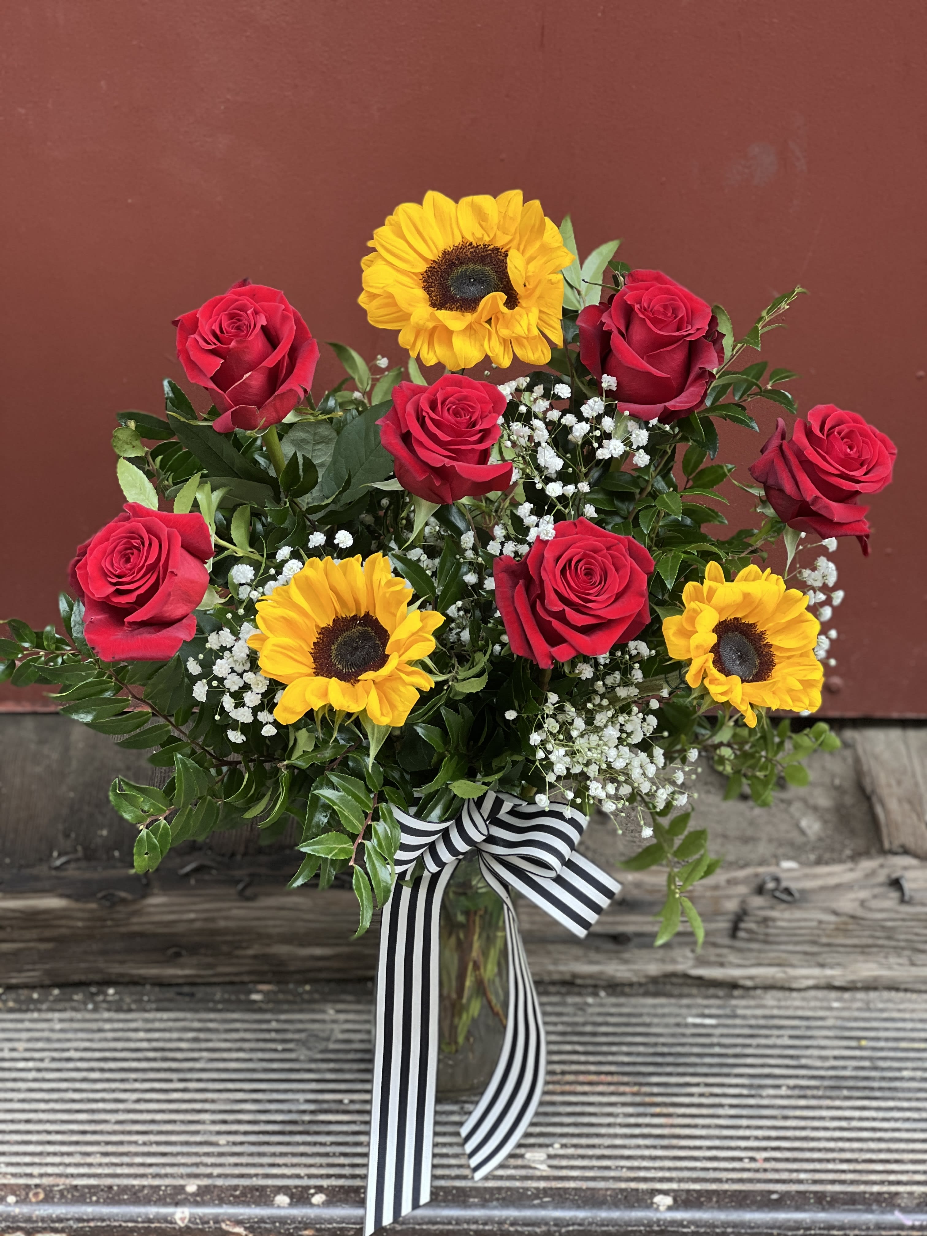 Roses &amp; Sunflowers - Beautiful mix of Red roses, sunflowers, babys breath and greenery, hand crafted in a vase with ribbon accent.  *Measures 18in tall, 8in wide
