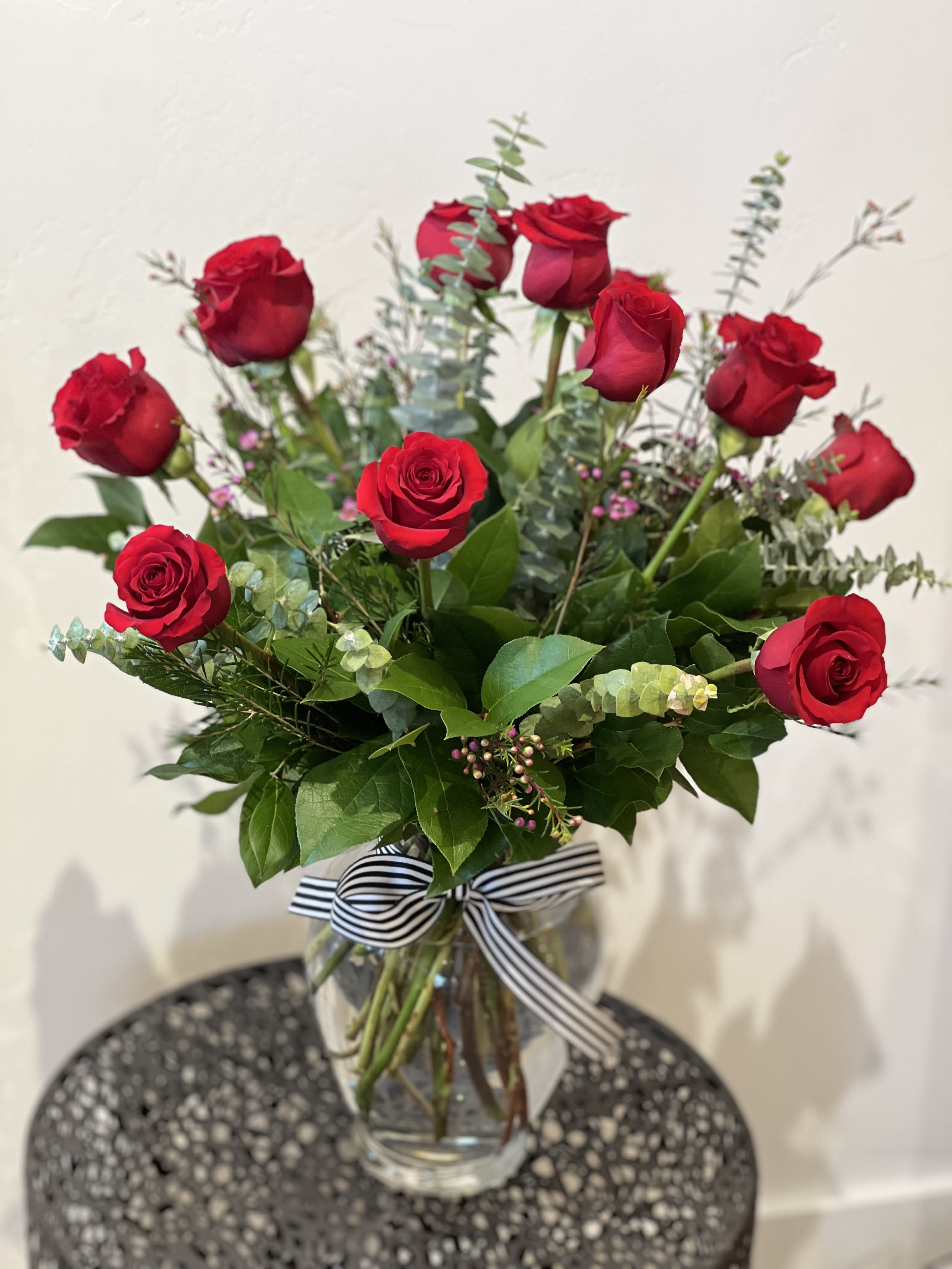 Dozen Red Rose Arrangement  - One dozen arranged fresh and crisp red roses designed in lush greens and fragrant spiral eucalyptus. Finished off with wax flower and our signature striped ribbon. 