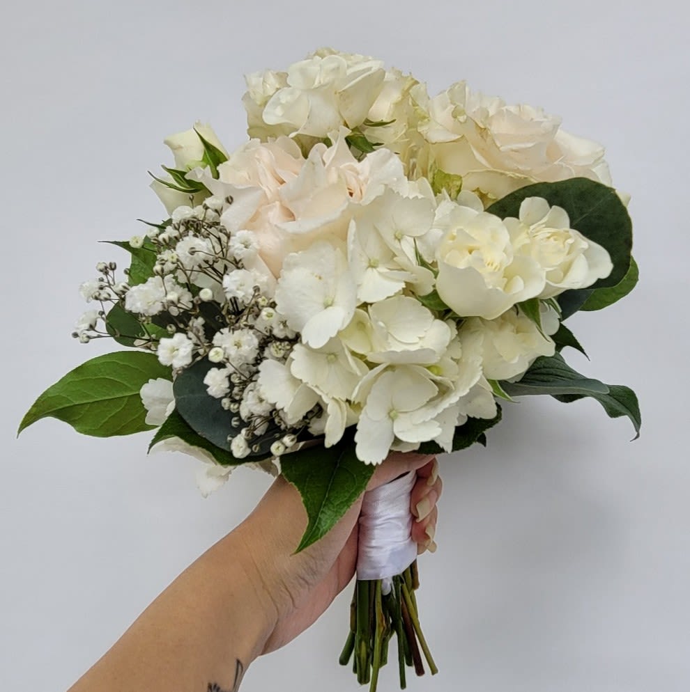 Nosegay in Blush - Nosegay in Blush Celebrate elegance and sophistication with our Nosegay in Blush, a hand-held bouquet designed to complement the most cherished occasions. Perfect for proms, homecoming dances, recitals, and weddings, this bouquet exudes timeless beauty and grace. ***Luxurious Composition: Featuring a lush base of white hydrangea, accented with open premium roses, garden roses, and tiny spray roses, this arrangement is a harmonious blend of texture and depth. ***Delicate Details: Filler accents and natural greenery add an organic touch, creating a bouquet that feels both refined and nature-inspired. ***Versatile Elegance: Elegantly bound in ivory ribbon, this bouquet complements semi-formal and formal wear, from tea-length dresses and bridal gowns to evening wear. Each bouquet is meticulously hand-designed to ensure freshness and quality, making it a perfect choice for creating unforgettable memories.