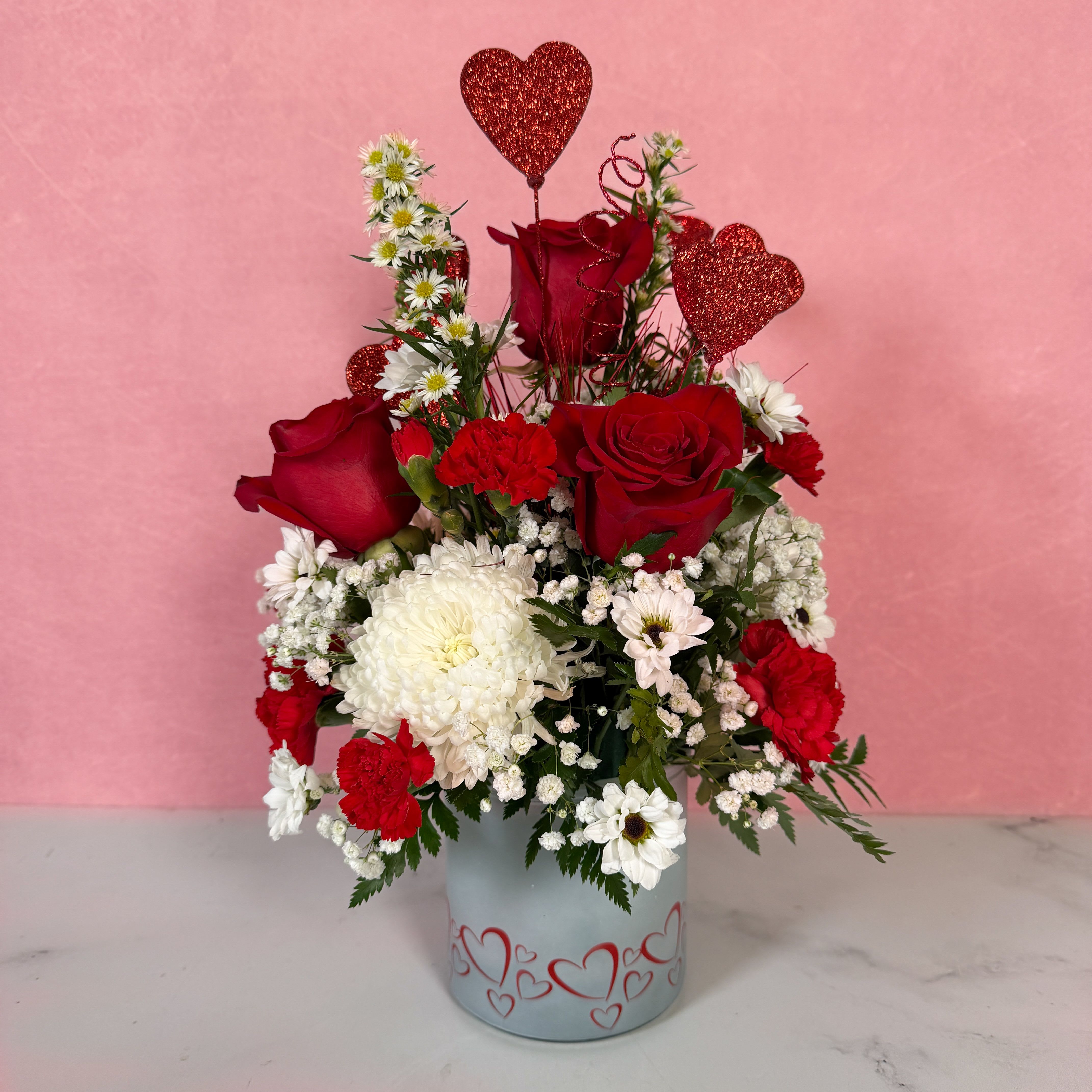 Blooming Hearts - Blooming Hearts is an impressive declaration of love! In this arrangement, red glittering hearts are blooming alongside red roses, carnations, white cremones, and yin yang daisies. The arrangement is artfully crafted in a glass vase adorned with red hearts, tying the whole piece together beautifully and making this a gift they won't forget!