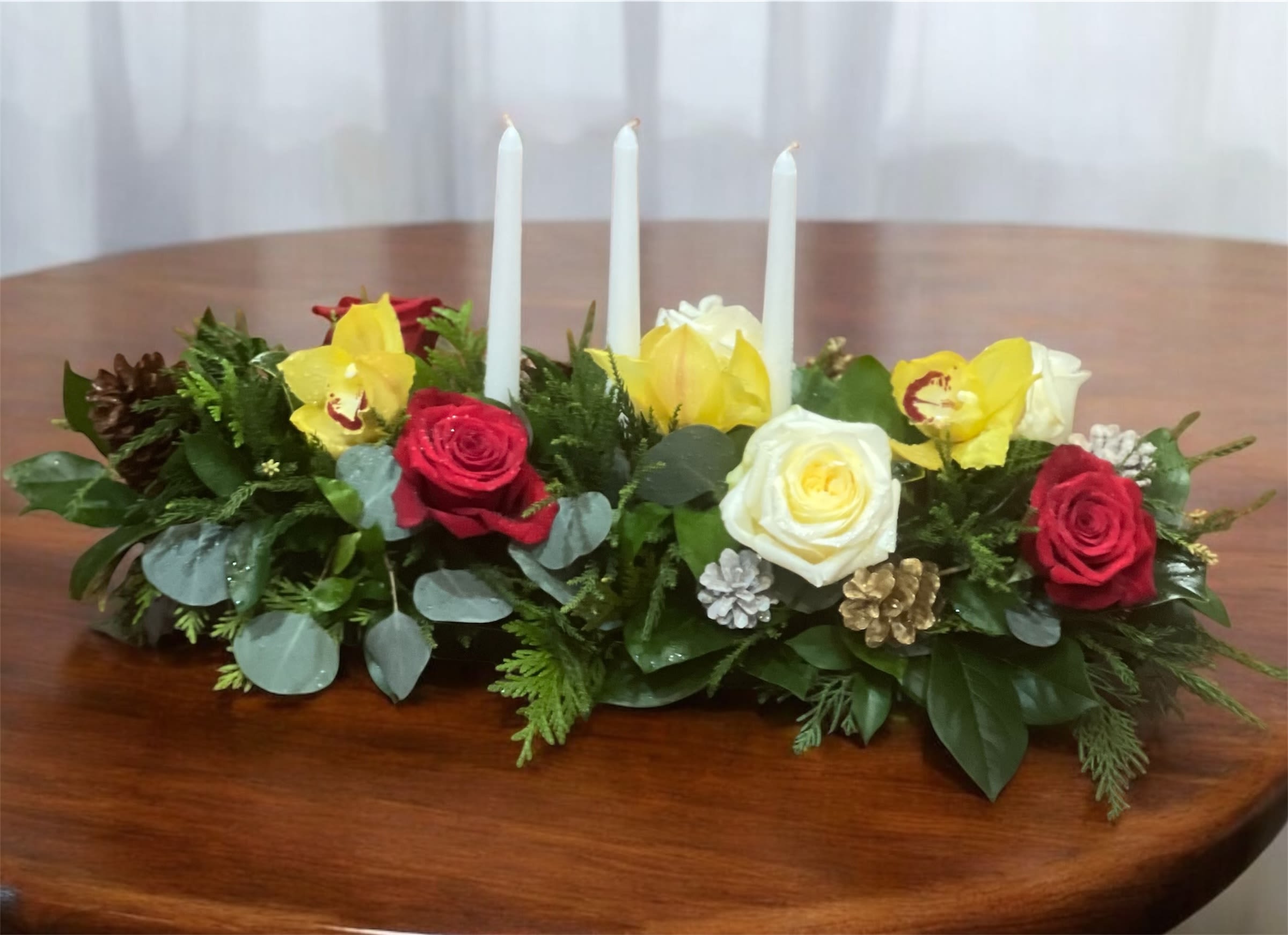 All is Bright - All is calm, all is bright… Gather family and friends together for a holiday meal around this traditional Christmas centerpiece featuring white and red roses, cymbidium orchids, and Christmas candles. 'Tis the season!