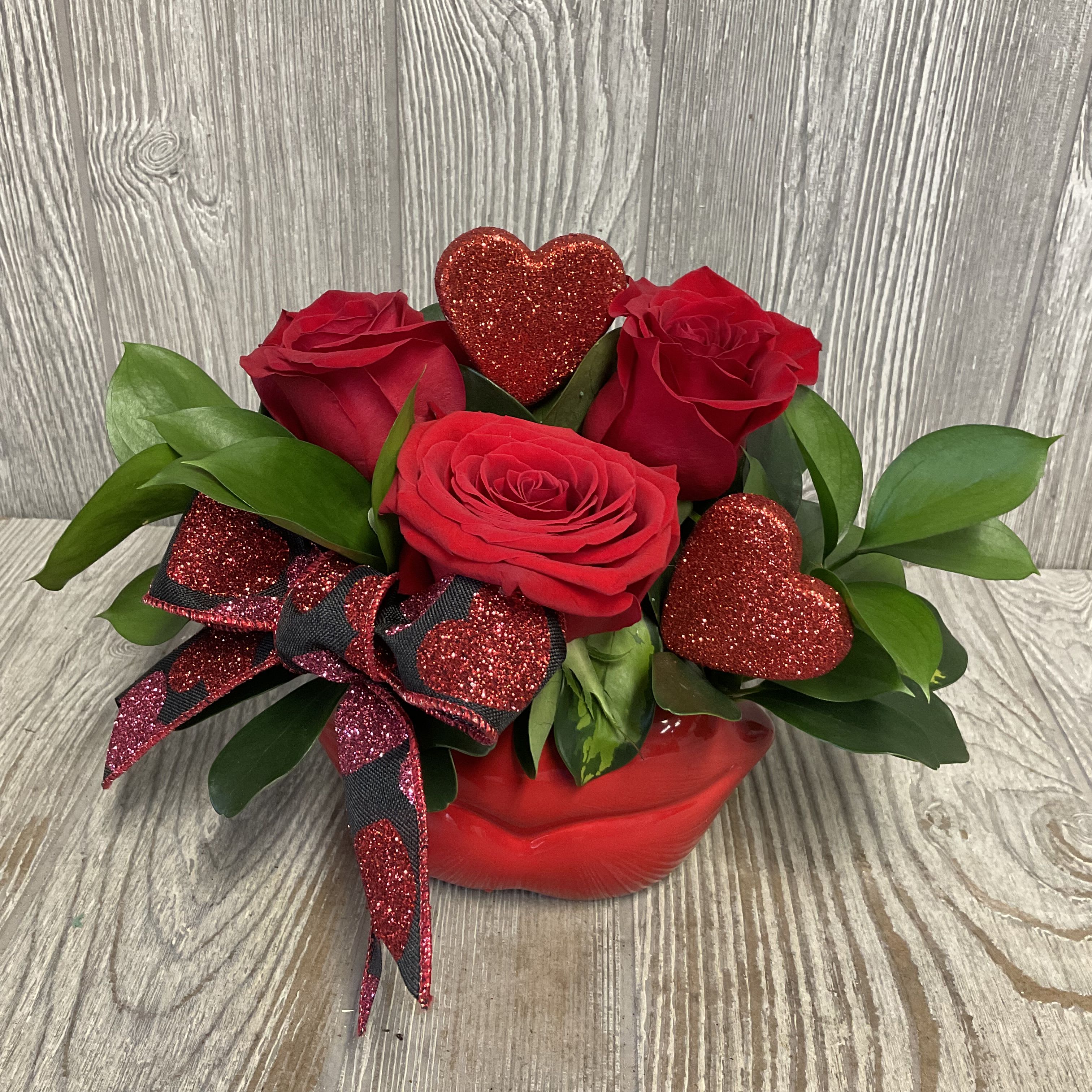 Pucker Up - A modern elegant arrangement of red roses in a keepsake ceramic lips container. Flowers and colors may vary. 