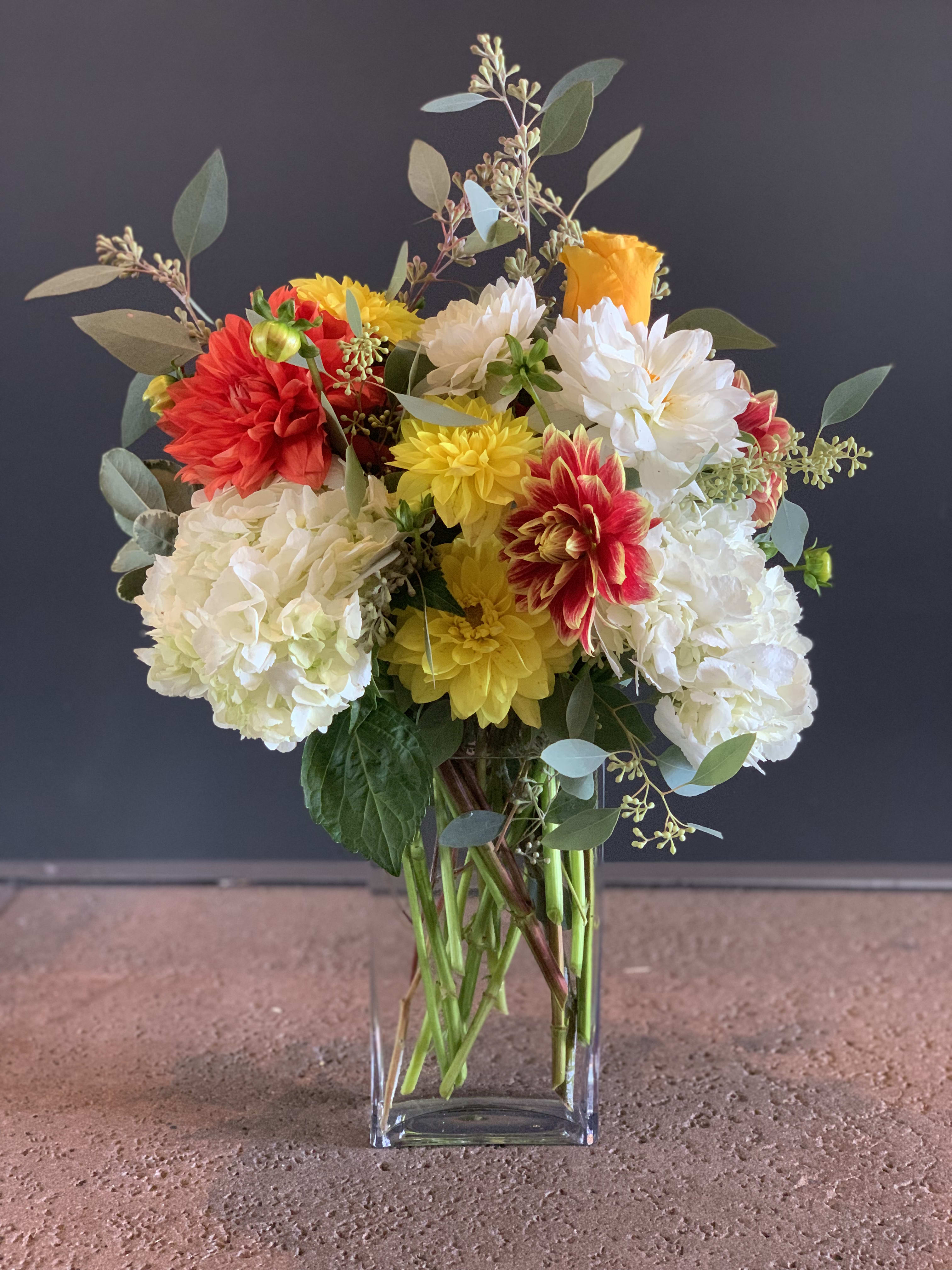 Dahlias Crush - A mix of colorful dahlias, white hydrangeas, seed eucalyptus in a clear glass vase.