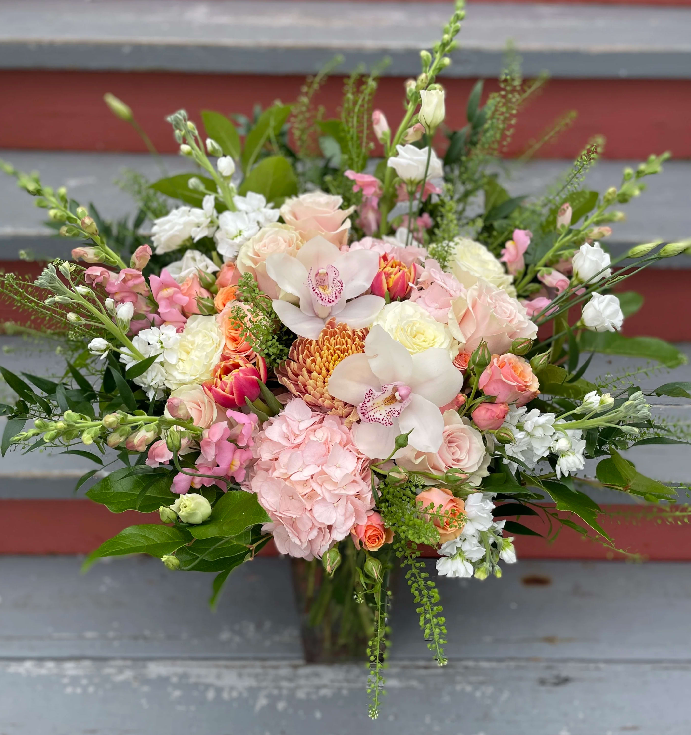 Passion in Bloom  - MINIMUM OF 24 HOURS NOTICE. A tall and lush arrangement for a big impression. A lovely 10 1/2" vase bursting with a variety of florals in various shades of pink (combo red and pink also available). features hydrangea, snapdragons, cymbidium orchids, roses, tulips and other seasonal textures. 