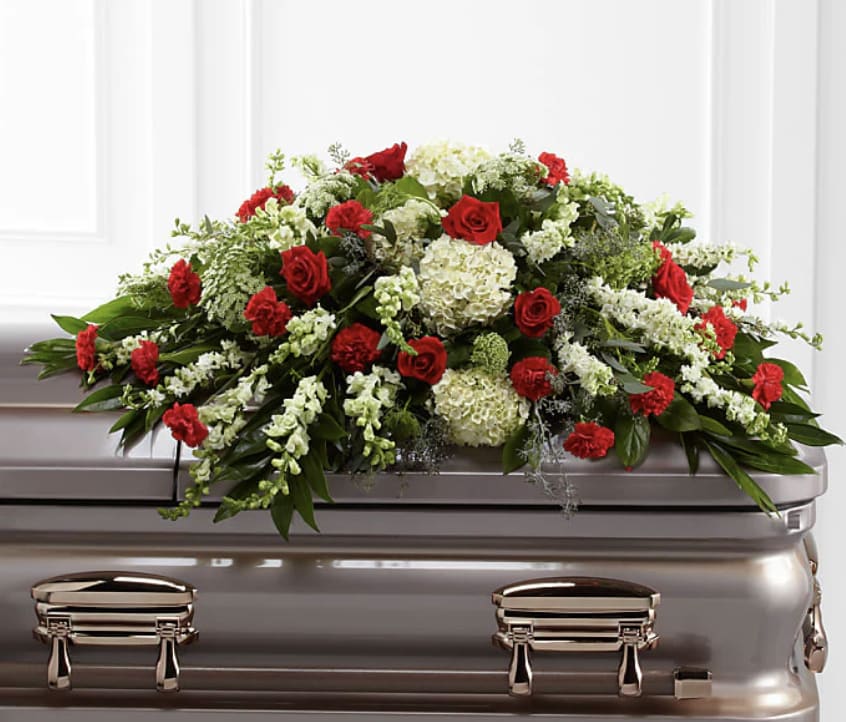 In Peace Casket Spray - This Casket Spray is a wondrous presentation of fresh color and beauty. Rich red roses and carnations are eye-catching and elegant in an arrangement of white hydrangea, larkspur, snapdragons, Queen Anne's Lace and assorted lush greens to create a lovely display meant to bedeck the top of their casket, bringing comfort and peace to those grieving the loss of the departed.  This is approximately 30"H x 48"W. Designed by florists, ready to display.  Bloom Details Rose Hydrangea Larkspur Snapdragon Carnation Queen Anne's Lace 