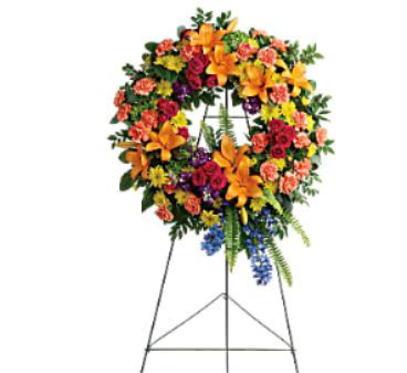 Colorful Serenity Wreath - This wreath features green hydrangea, hot pink spray roses, orange asiatic lilies, orange carnations, blue delphinium, purple stock, yellow cushion spray chrysanthemums, huckleberry, variegated pittosporum, sword fern, silver dollar eucalyptus, and lemon leaf. Delivered on a wire easel.