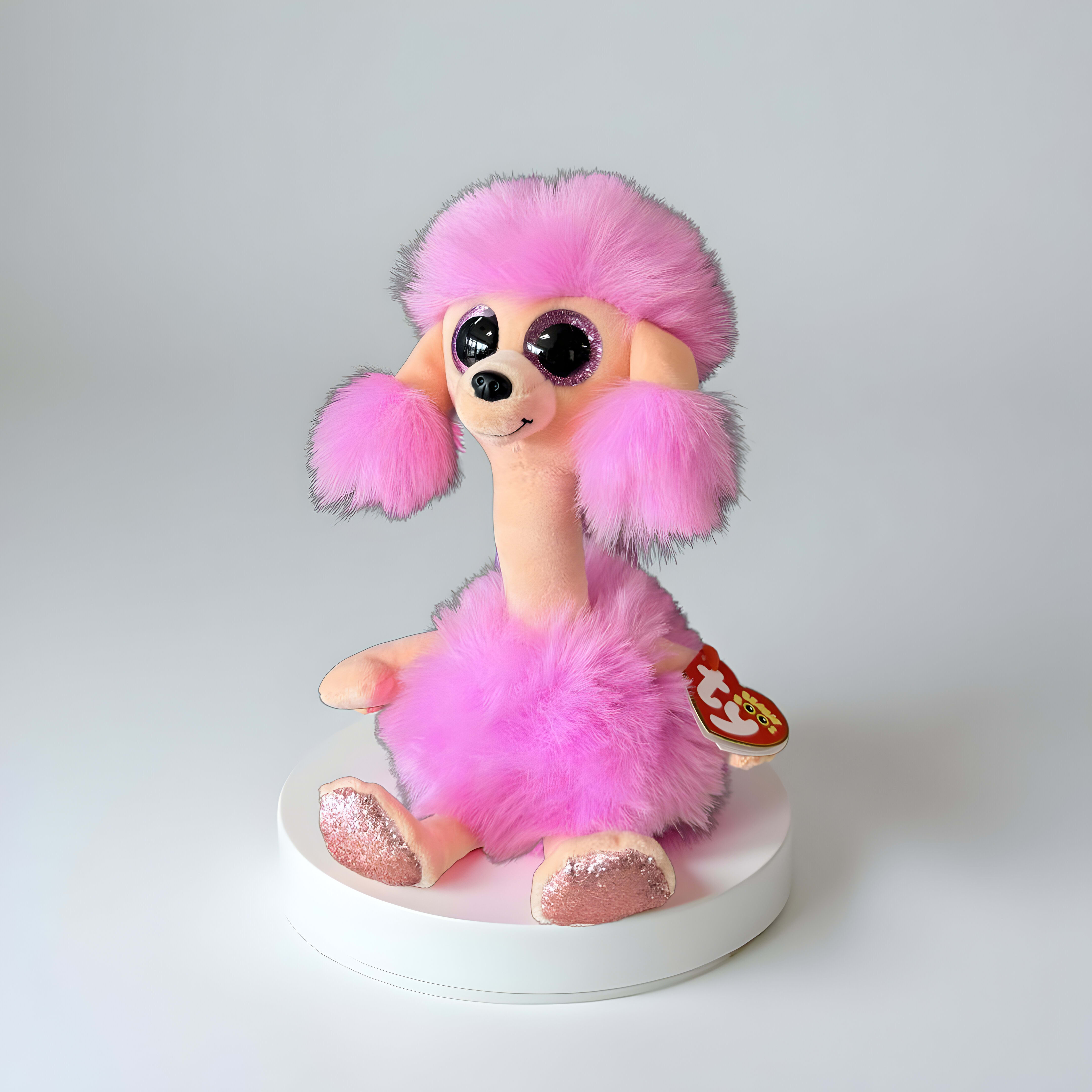 Camilla - This product is a Ty Beanie Boos Camilla the Pink Poodle plush toyIt is a bright pink poodle with large, captivating sparkly glitter eyes and a matching pink glitter nose. It has a long, slender neck and textured, fluffy pink faux fur accents on its head, ears, neck, and torso, giving it a classic poodle look. Its paws also feature pink sparkle accents.This toy is most commonly available in a regular 6-inch size.