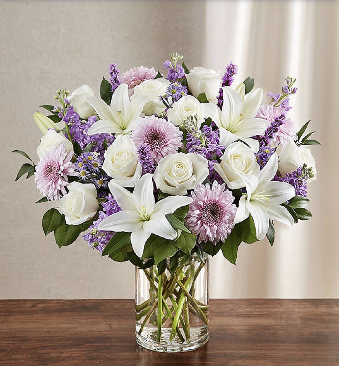 Sincerest Lavender &amp; White - Let a deeply heartfelt sentiment be delivered in true form. Our lush, bountiful bouquet of lavender and white blooms features an elegant mix of roses, lilies and mums, hand-designed inside a classic clear glass vase. When sent to a service or to the home of family or friends, it makes a genuinely heartwarming gesture.