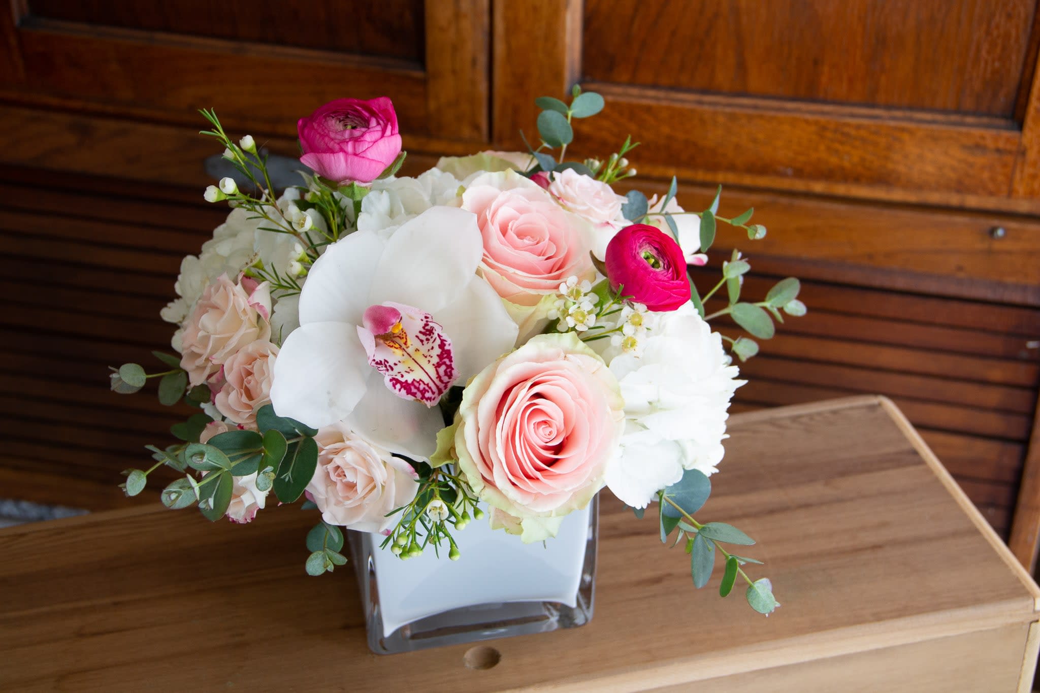 Little Bundle of Love: Red or Pink - A compact, more modern style arrangement featuring roses, spray roses, hydrangea, and a beautiful orchid accent. This arrangement comes in a lovely white glass cube vase and is a perfect size for the nightstand or coffee table. Please let us know what color profile you prefer: red, pink or a combination in the notes. If no choice is given designer will decide