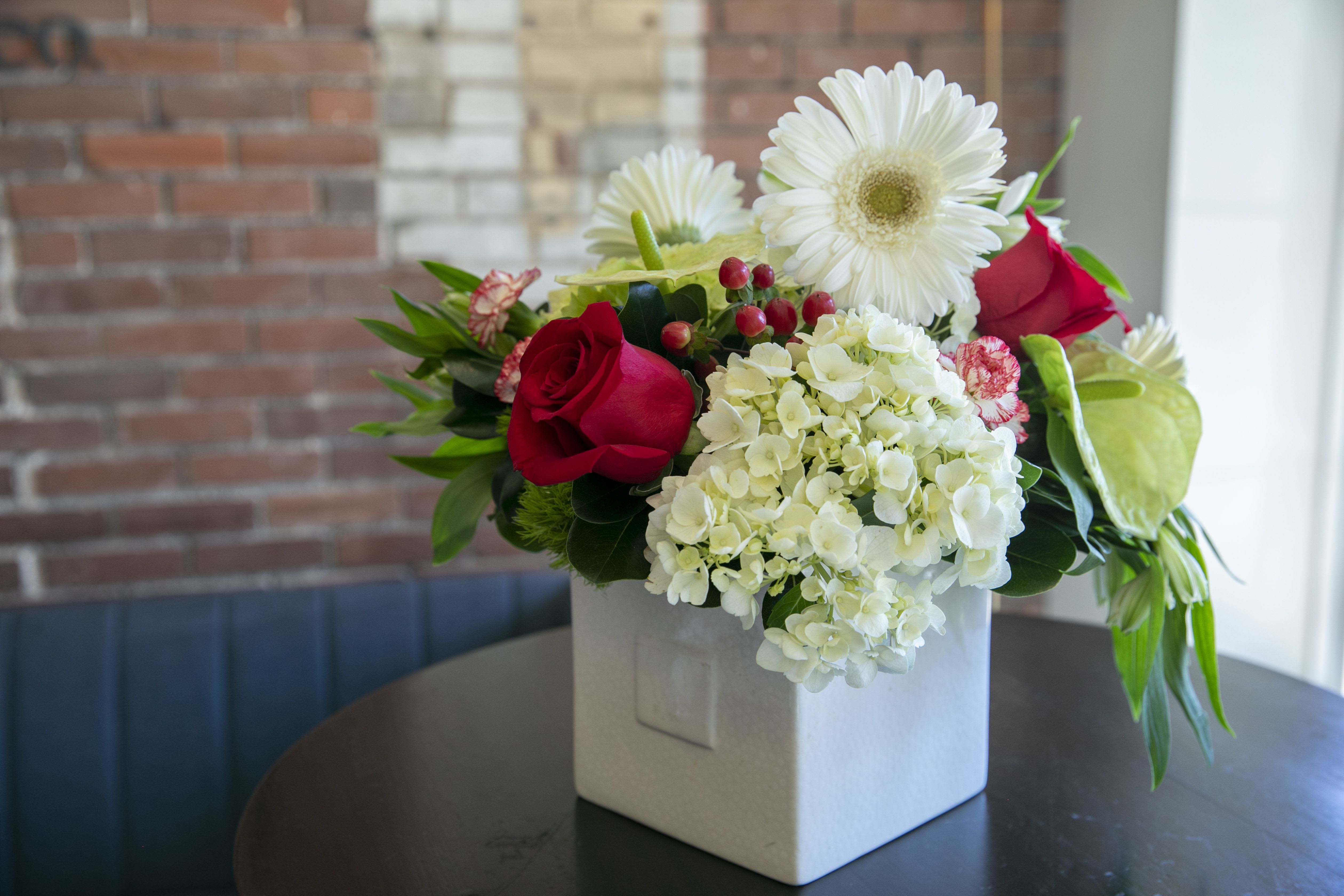 Amore - snow white hydrangeas with red rose, red berries and white happy gerber daisies arranged in a glass square. perfect for table centerpiece, not too tall just right size for your dinner conversations during Valentine's day .