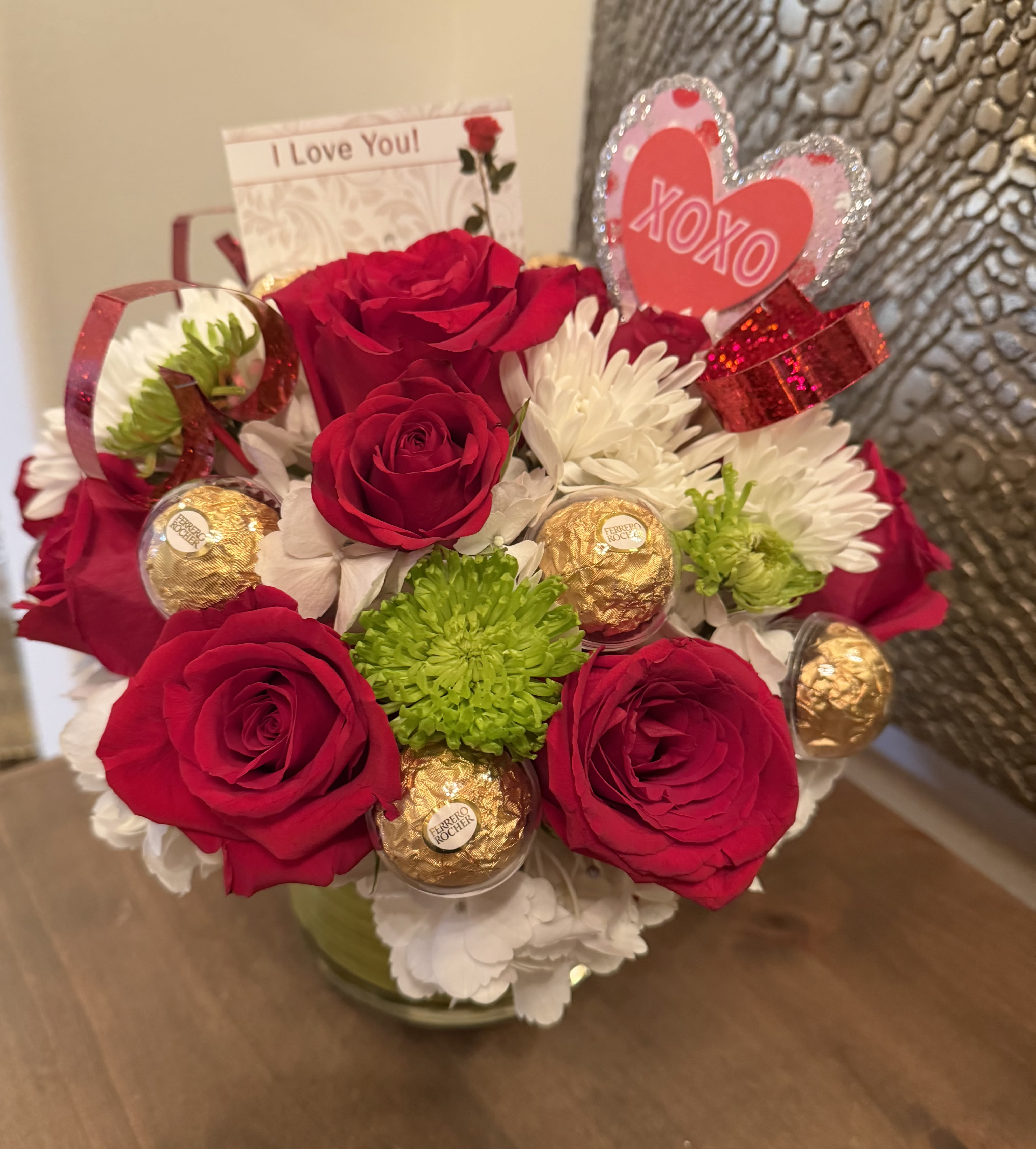 Love Bites - A romantic Valentine’s flower arrangement featuring lush red roses paired with cheerful mums and soft white hydrangeas, creating a beautiful balance of passion and elegance. Accented with indulgent Ferrero Rocher chocolates, this arrangement is the perfect expression of love, sweetness, and heartfelt celebration. ️. This arrangement has 10 premium red roses , white hydrangeas , white mums and 10 Ferrero Rocher chocolates.